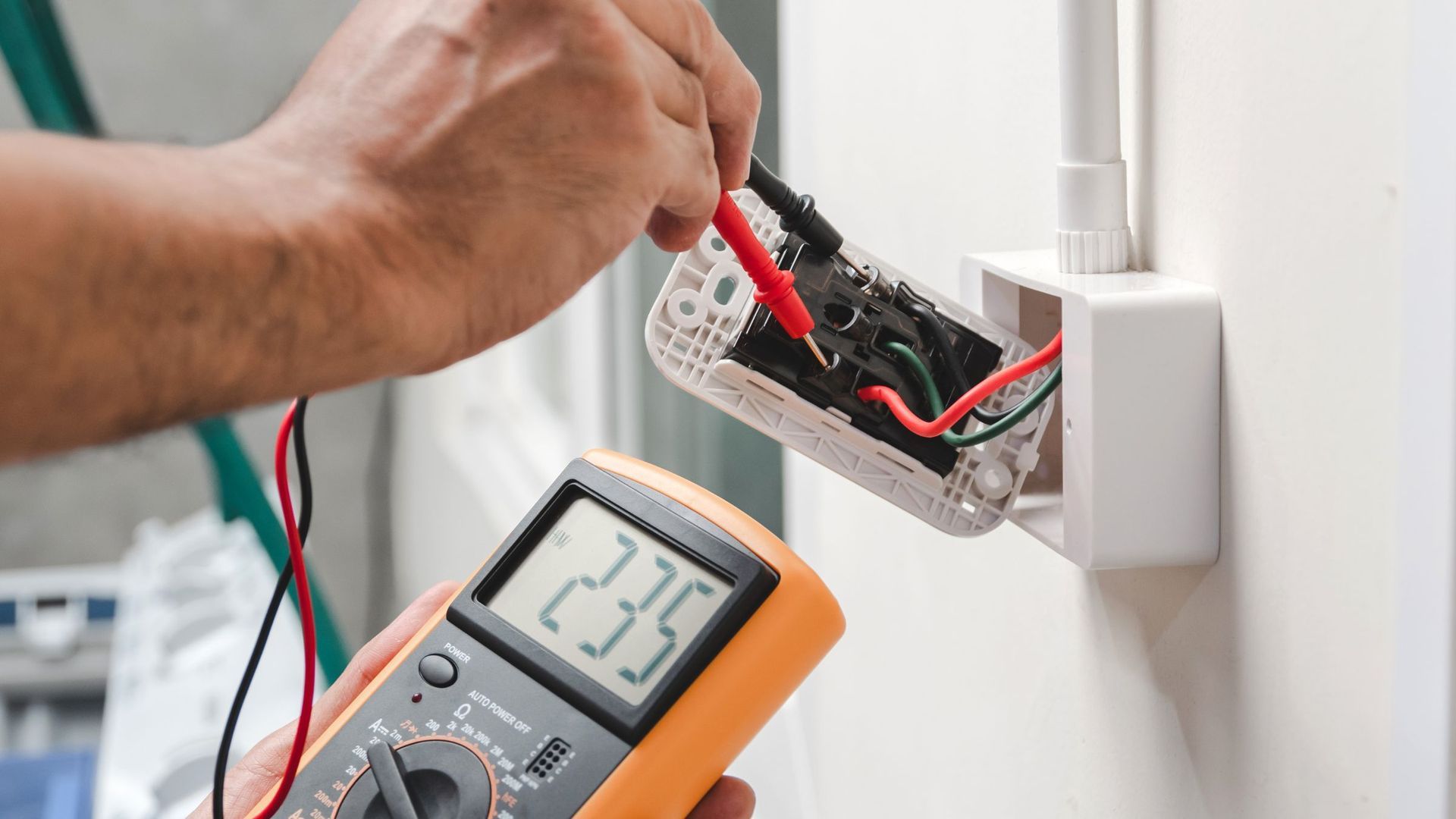 A person is using a multimeter to test an electrical outlet.