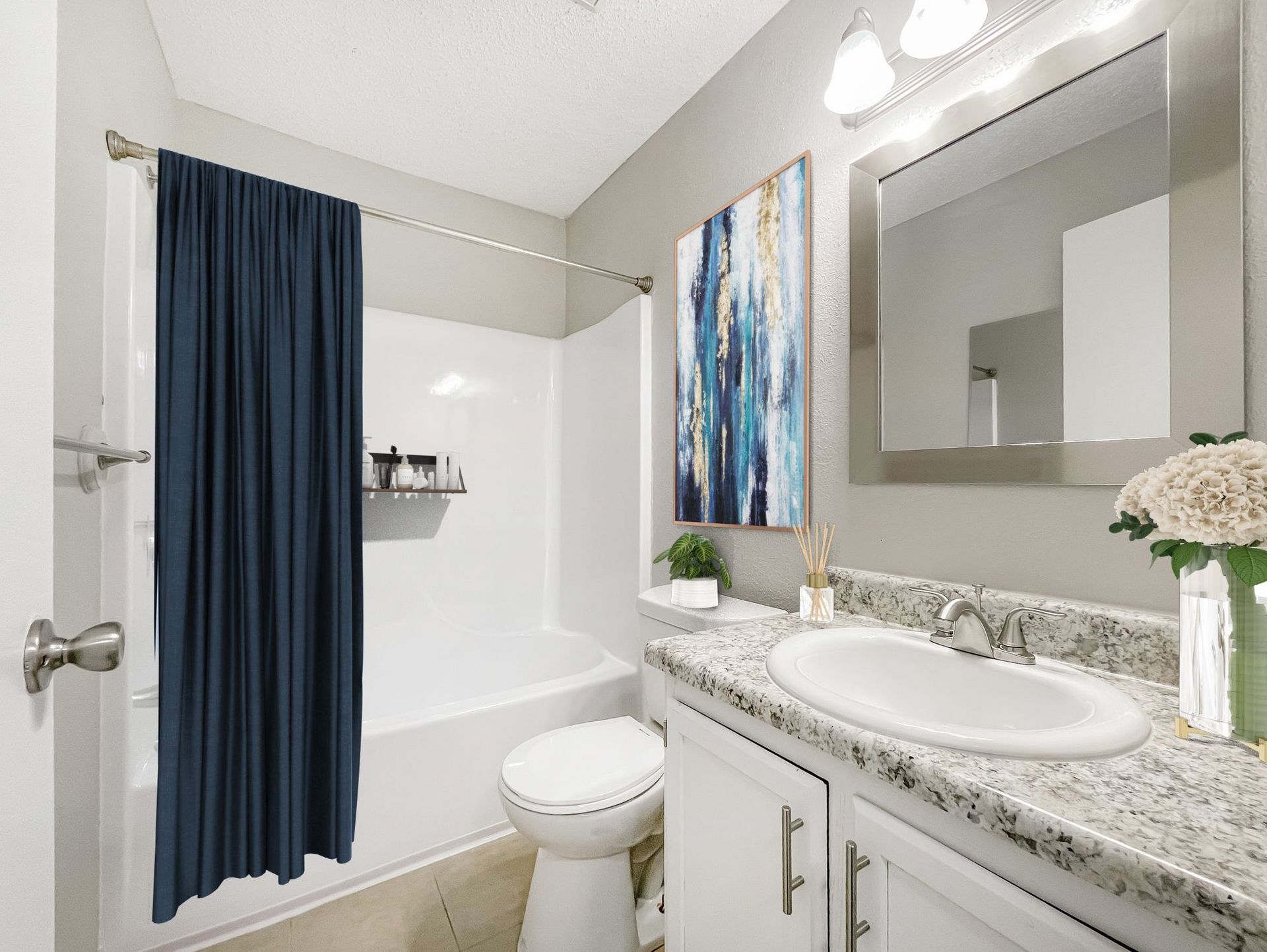 A modern bathroom with a navy shower curtain, white tub, toilet, granite vanity, and abstract blue and gold wall art.