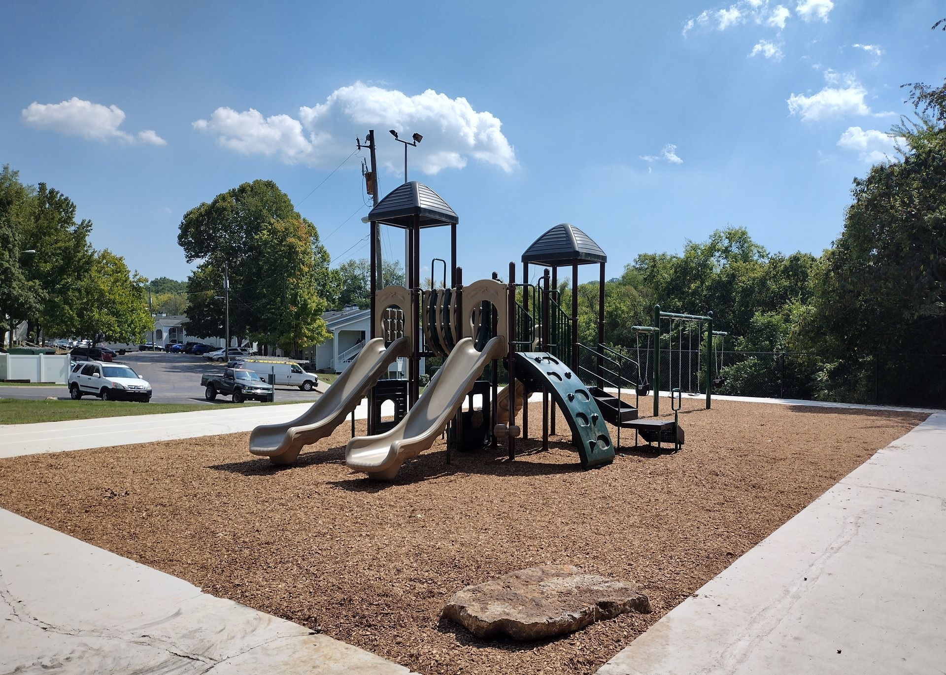A playground with two slides and a climbing wall set in a woodchip-covered area on a sunny day.