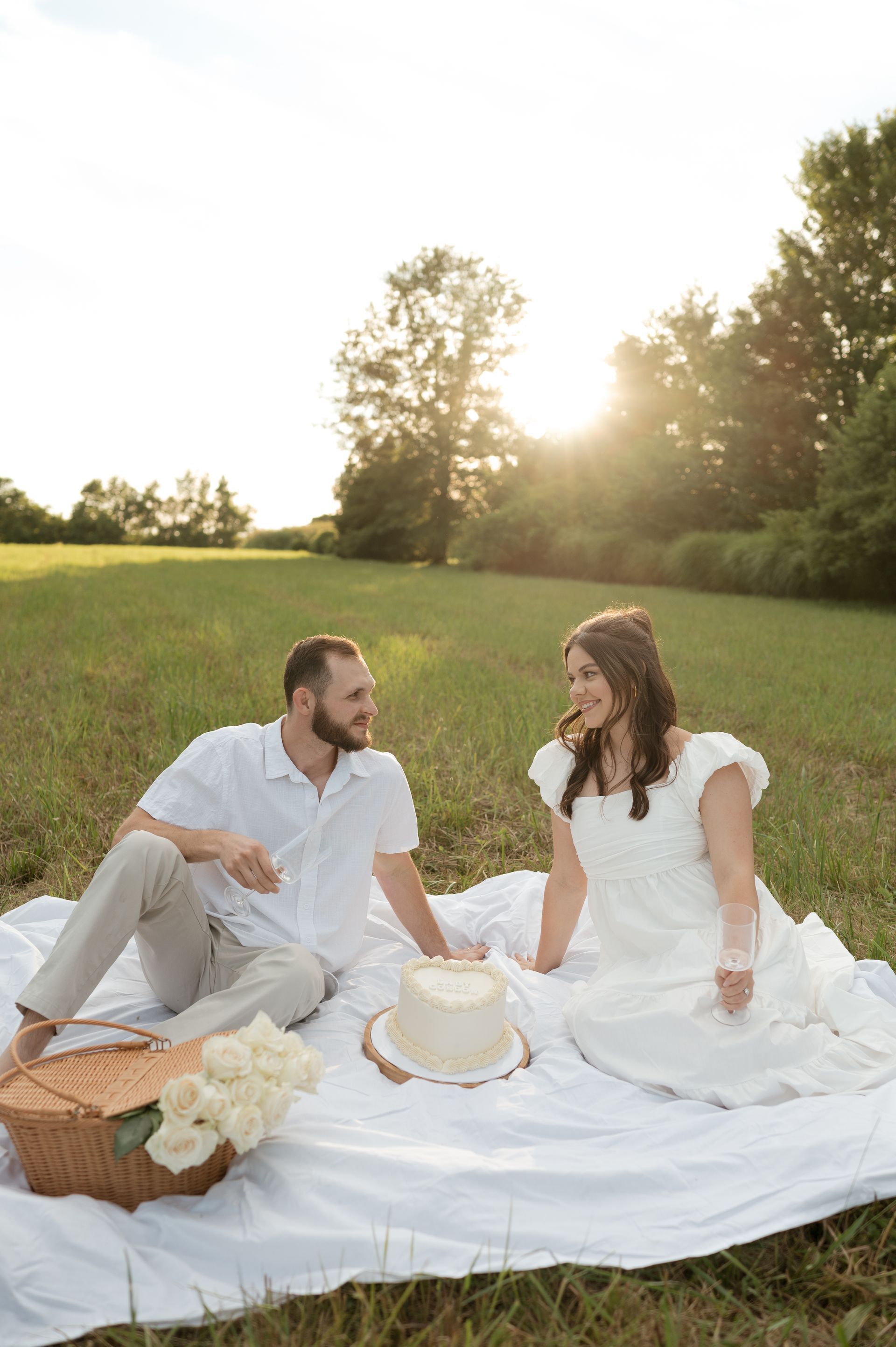 A man and a woman are sitting on a blanket in a field with a cake.