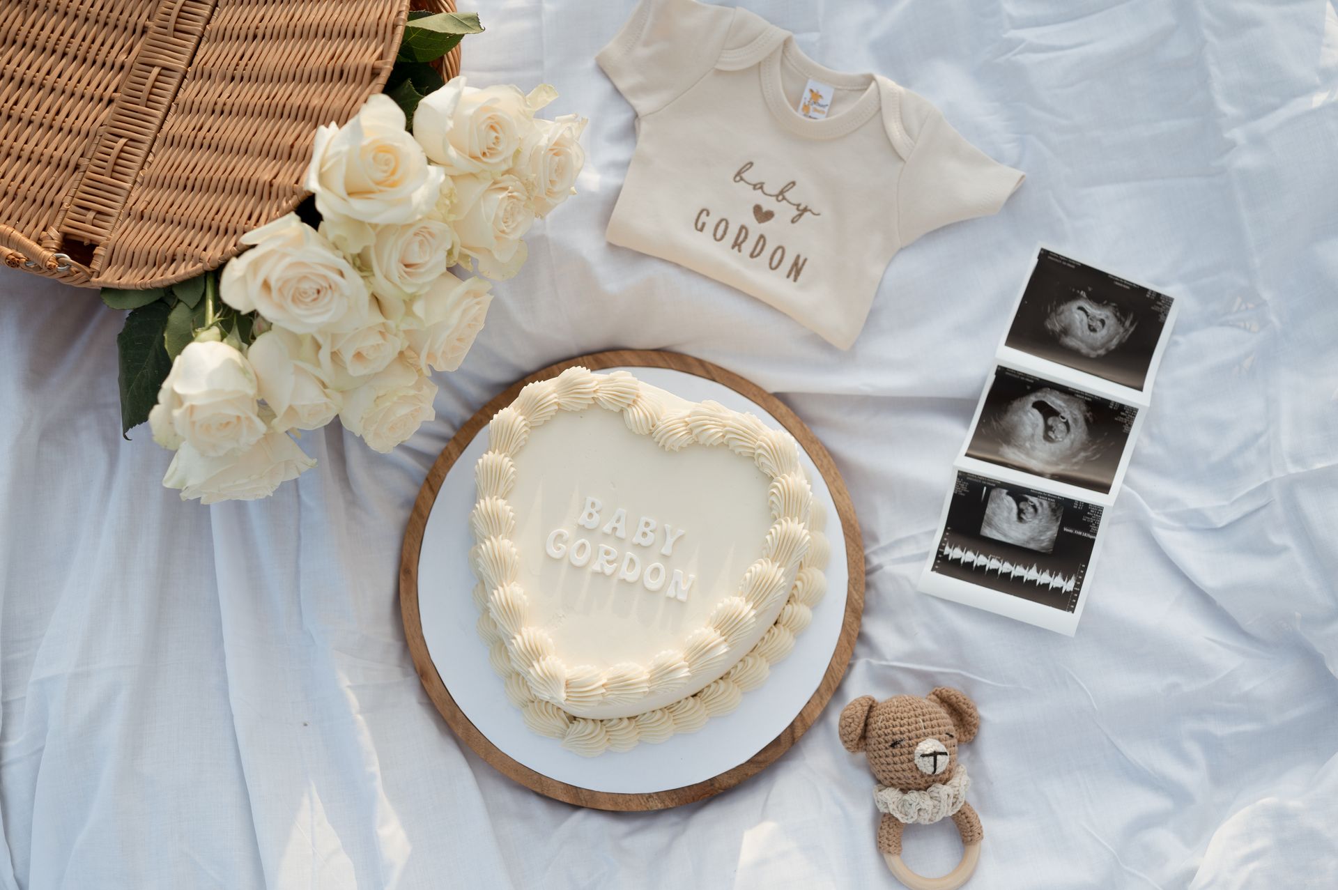 A heart shaped cake is sitting on a table next to a teddy bear and a baby shirt.