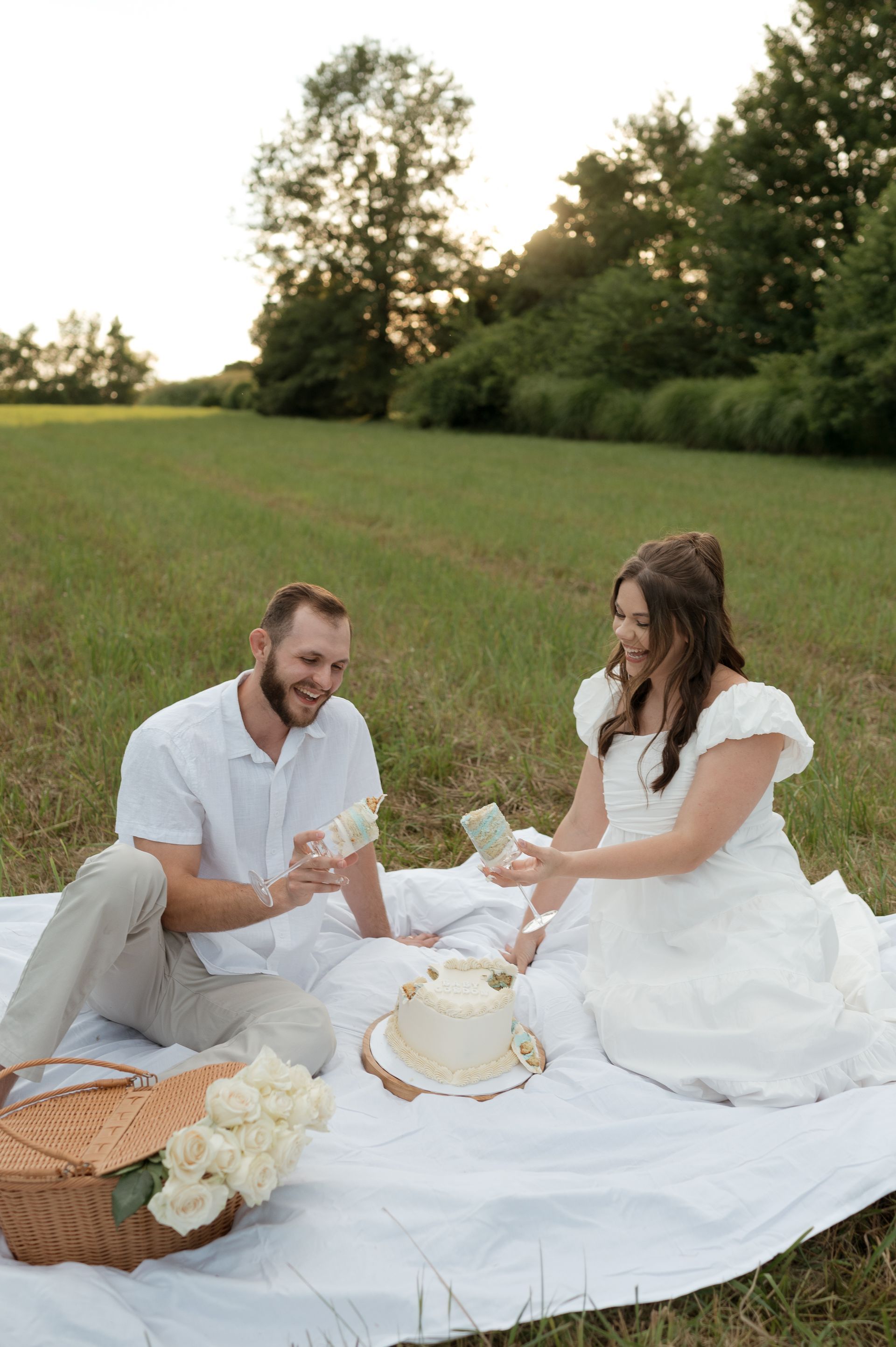 A man and a woman are sitting on a blanket in a field with a cake.