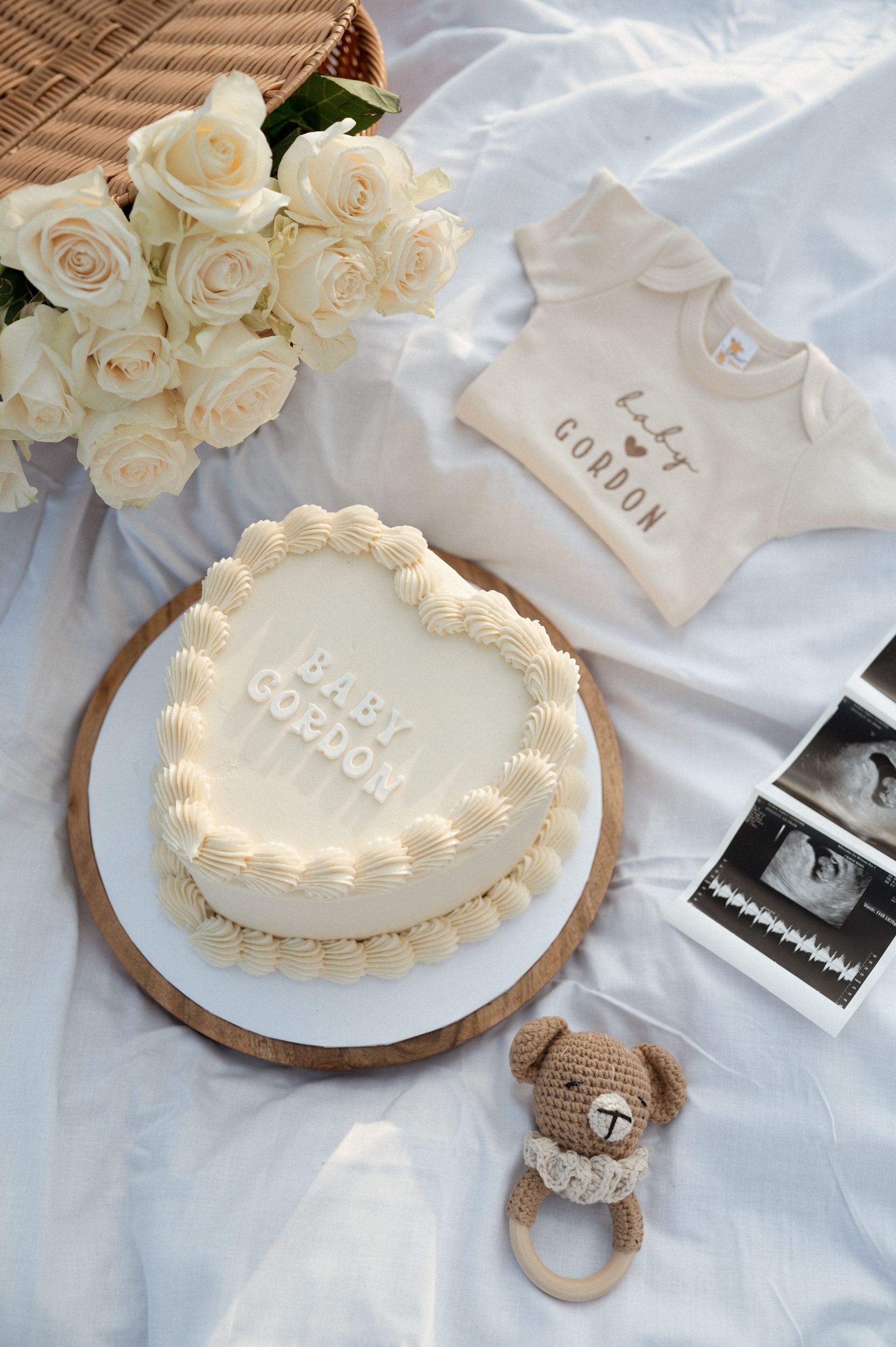 A cake is sitting on a table next to a baby shirt and a teddy bear.