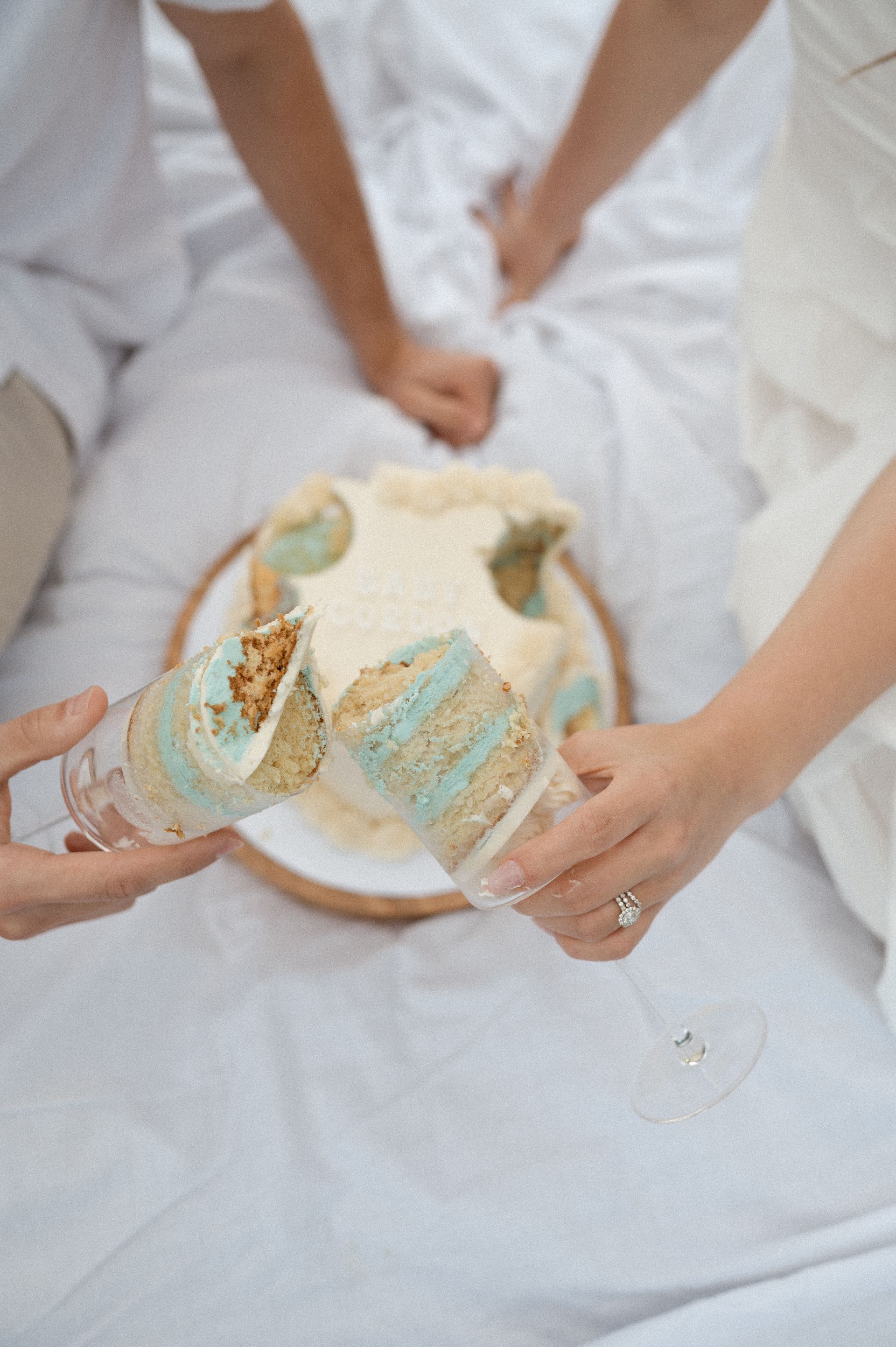 A couple is sitting on a bed eating a cake and drinking champagne.