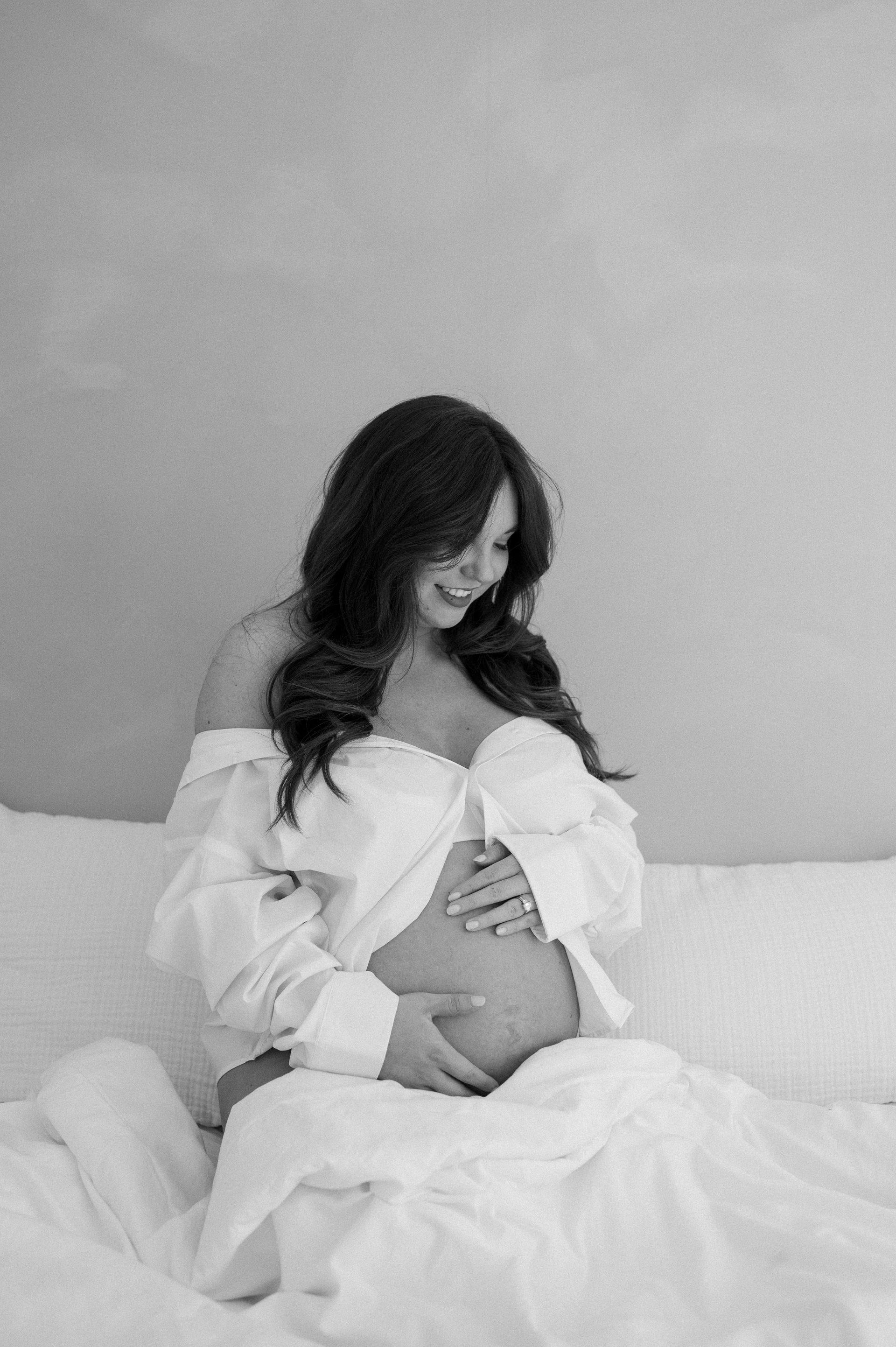 A pregnant woman is sitting on a bed holding her belly.