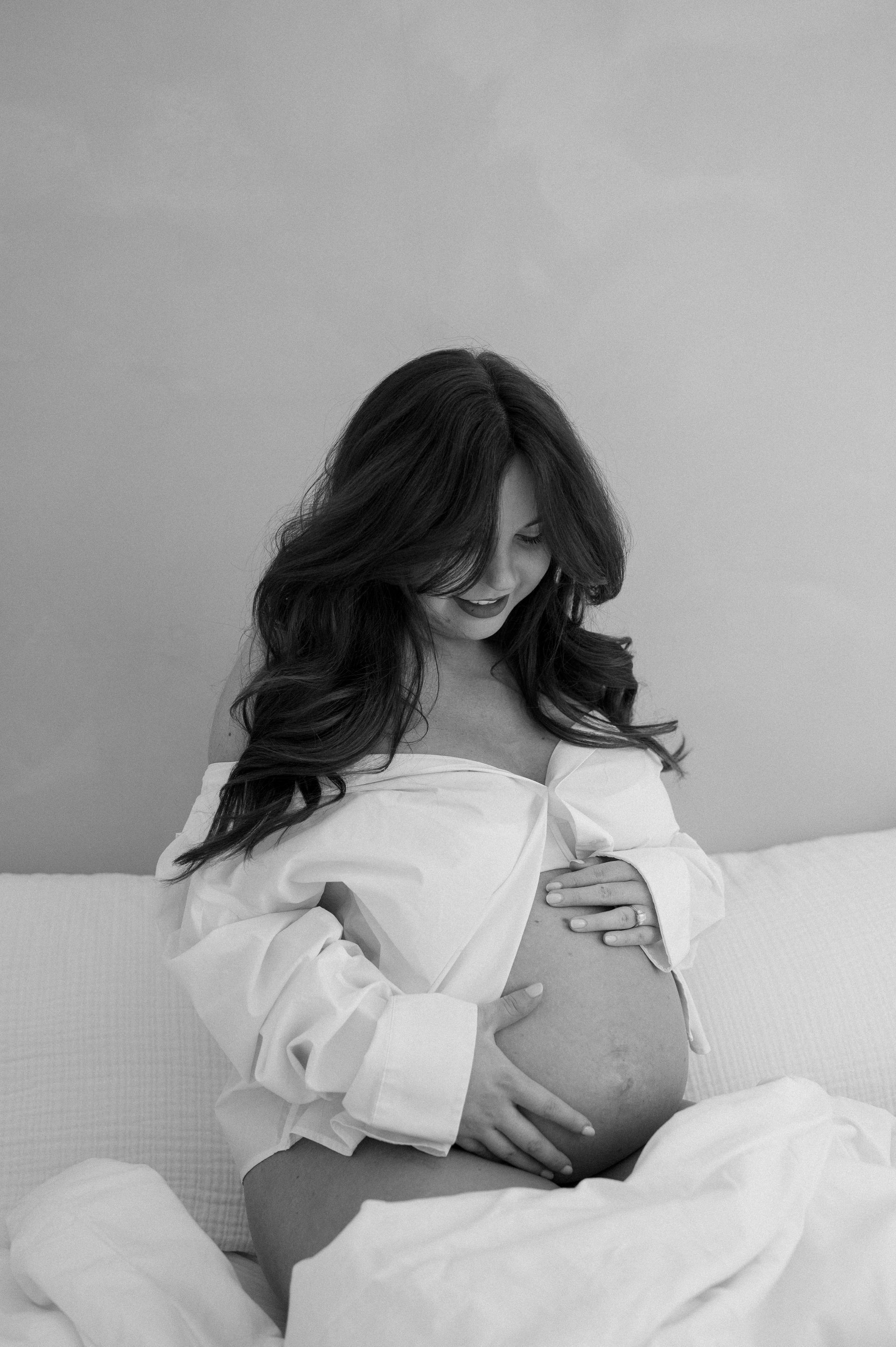 A pregnant woman is sitting on a bed holding her belly.