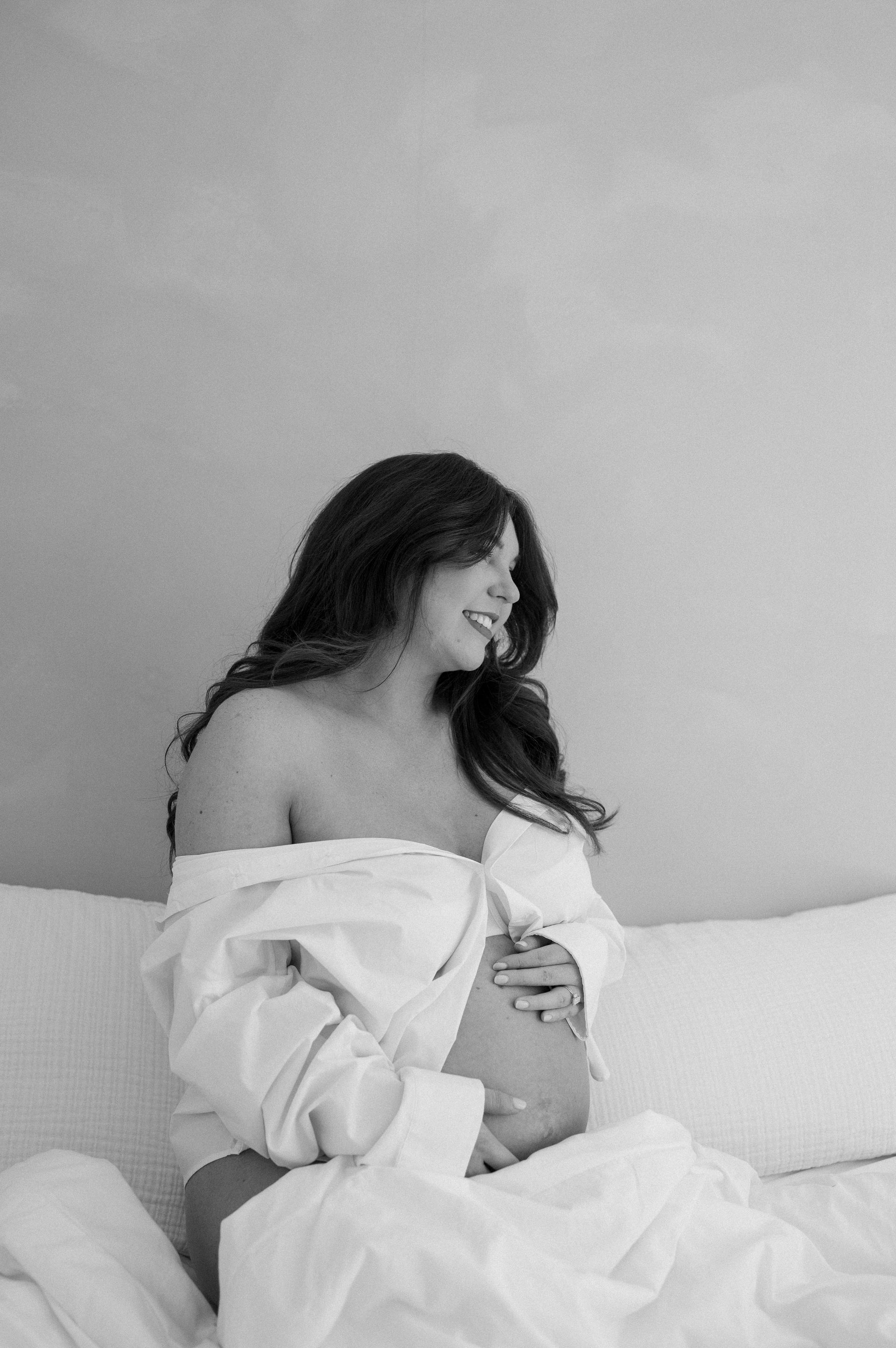 A pregnant woman is sitting on a bed holding her belly.
