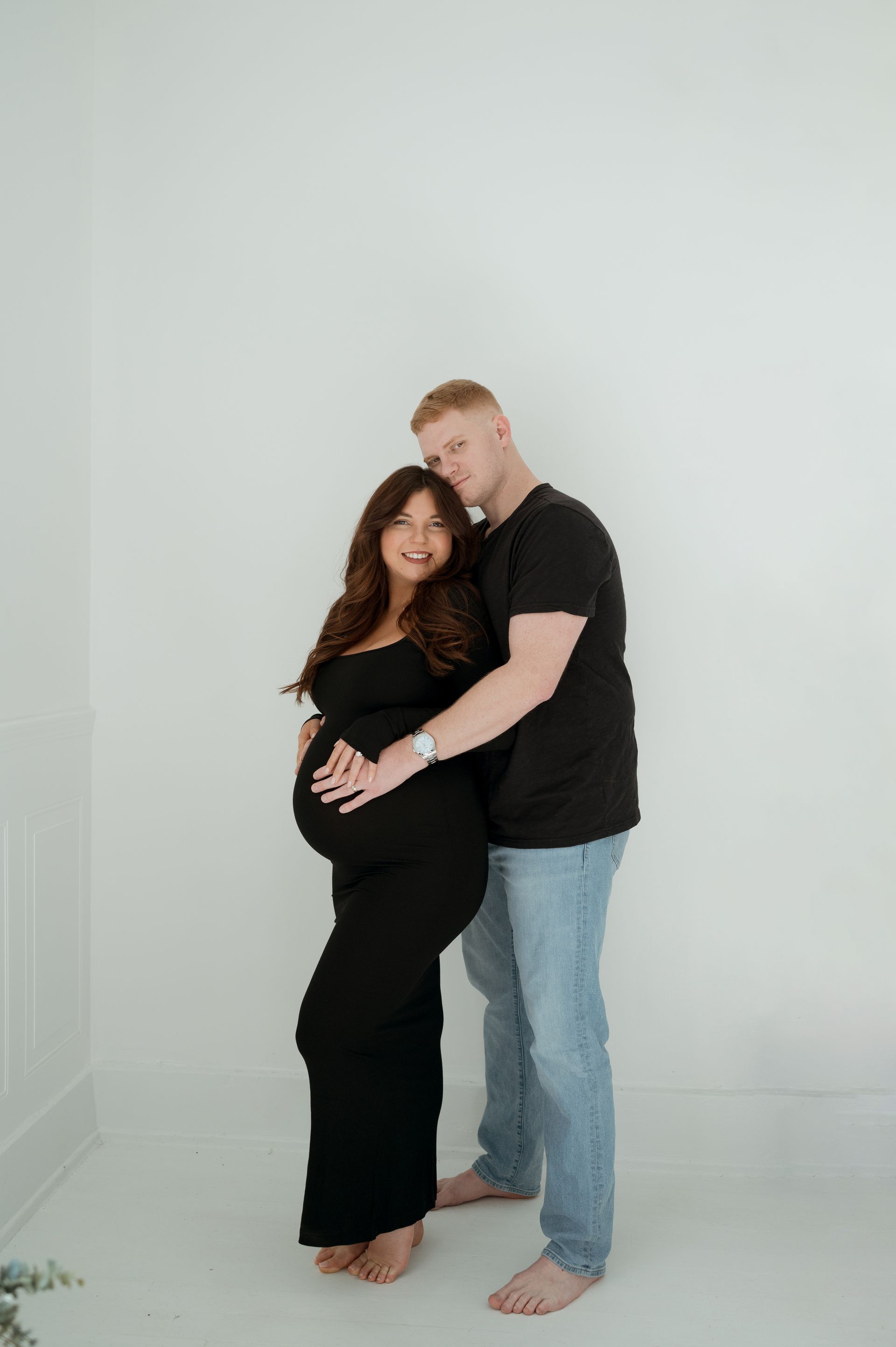 A man is hugging a pregnant woman in a black dress.