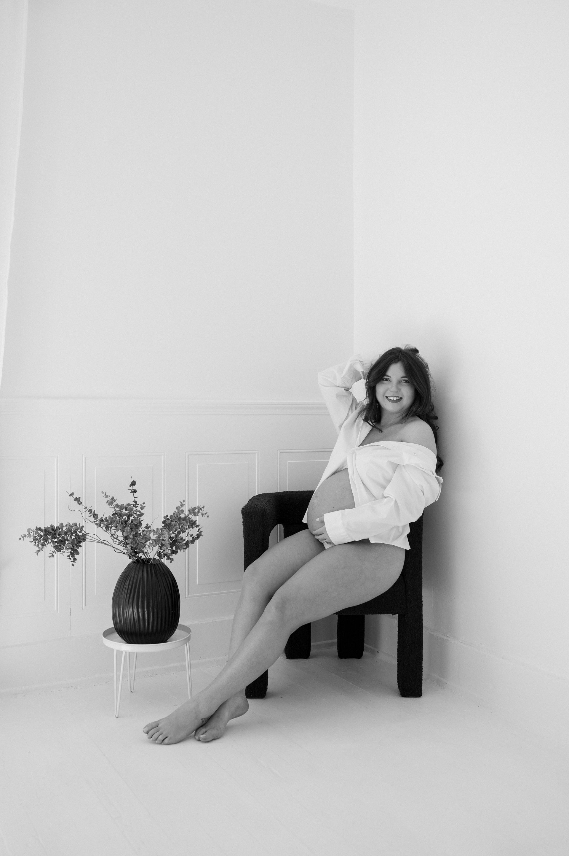 A pregnant woman is sitting in a chair in a black and white photo.