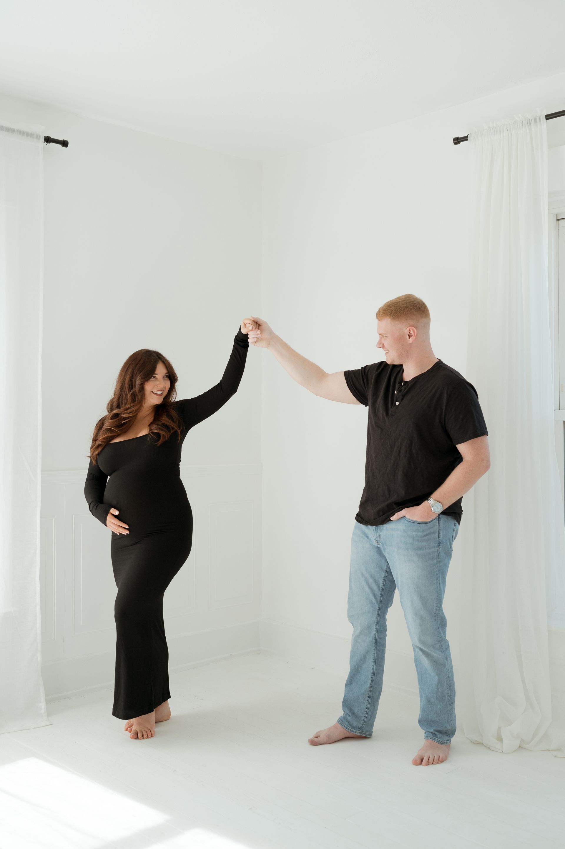 A man and a pregnant woman are dancing in a white room.