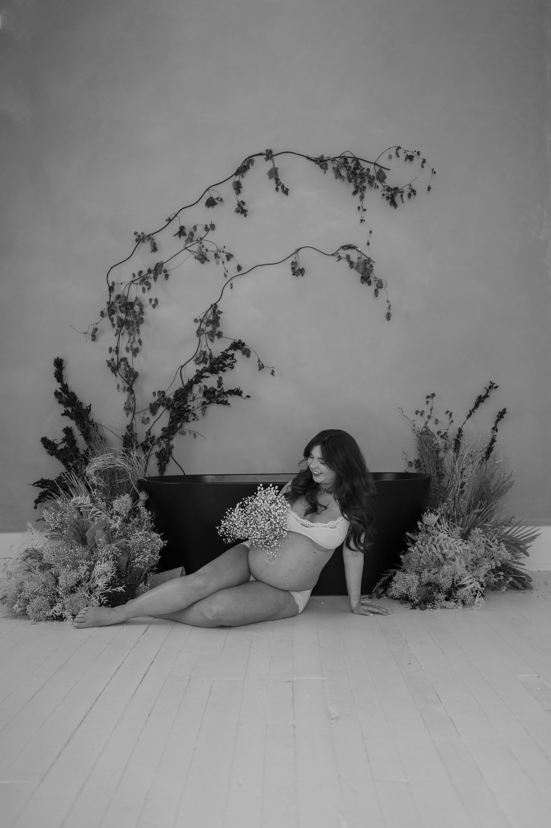 A pregnant woman is sitting on the floor holding a bouquet of flowers.