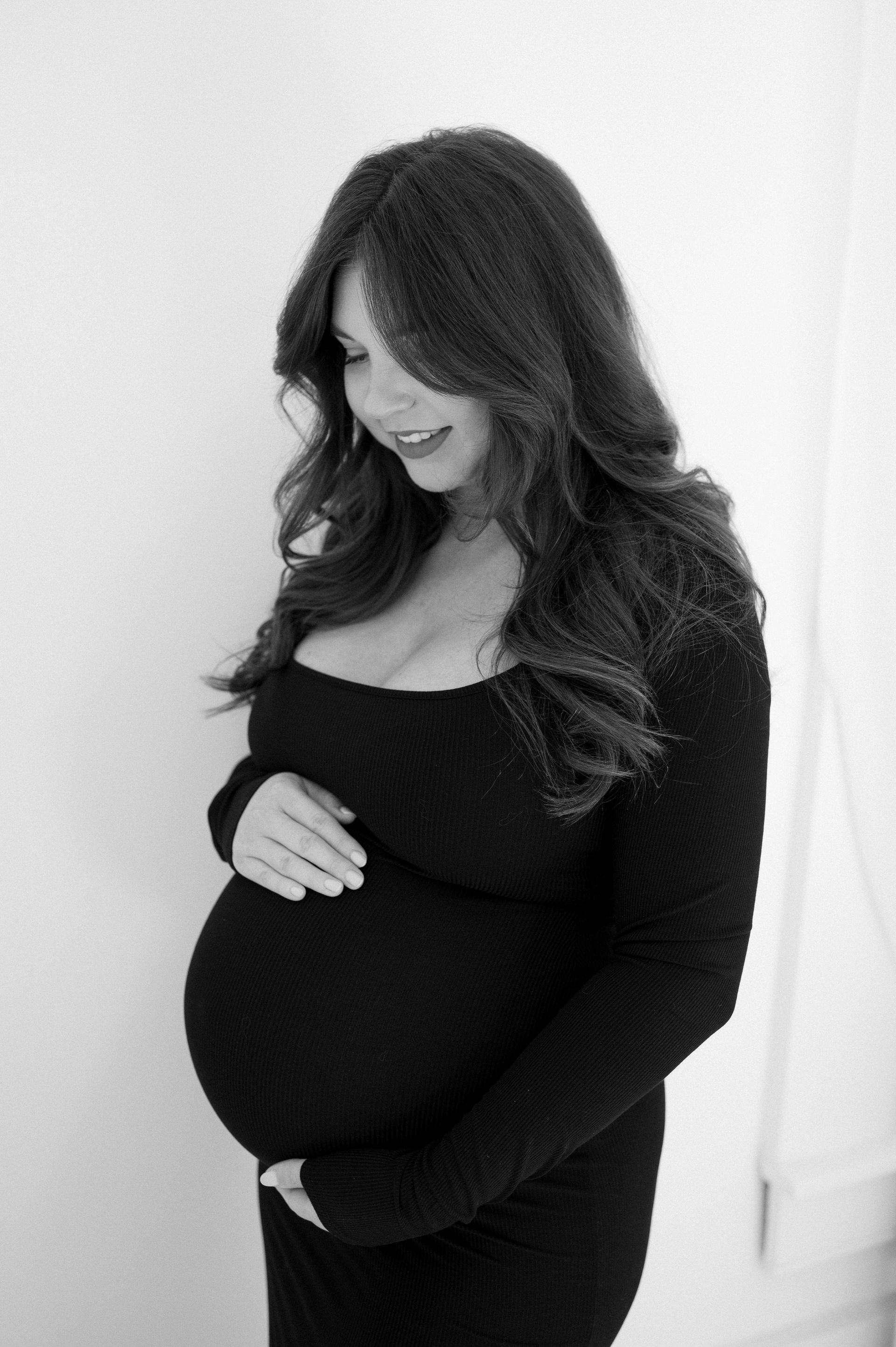 A pregnant woman in a black dress is holding her belly.
