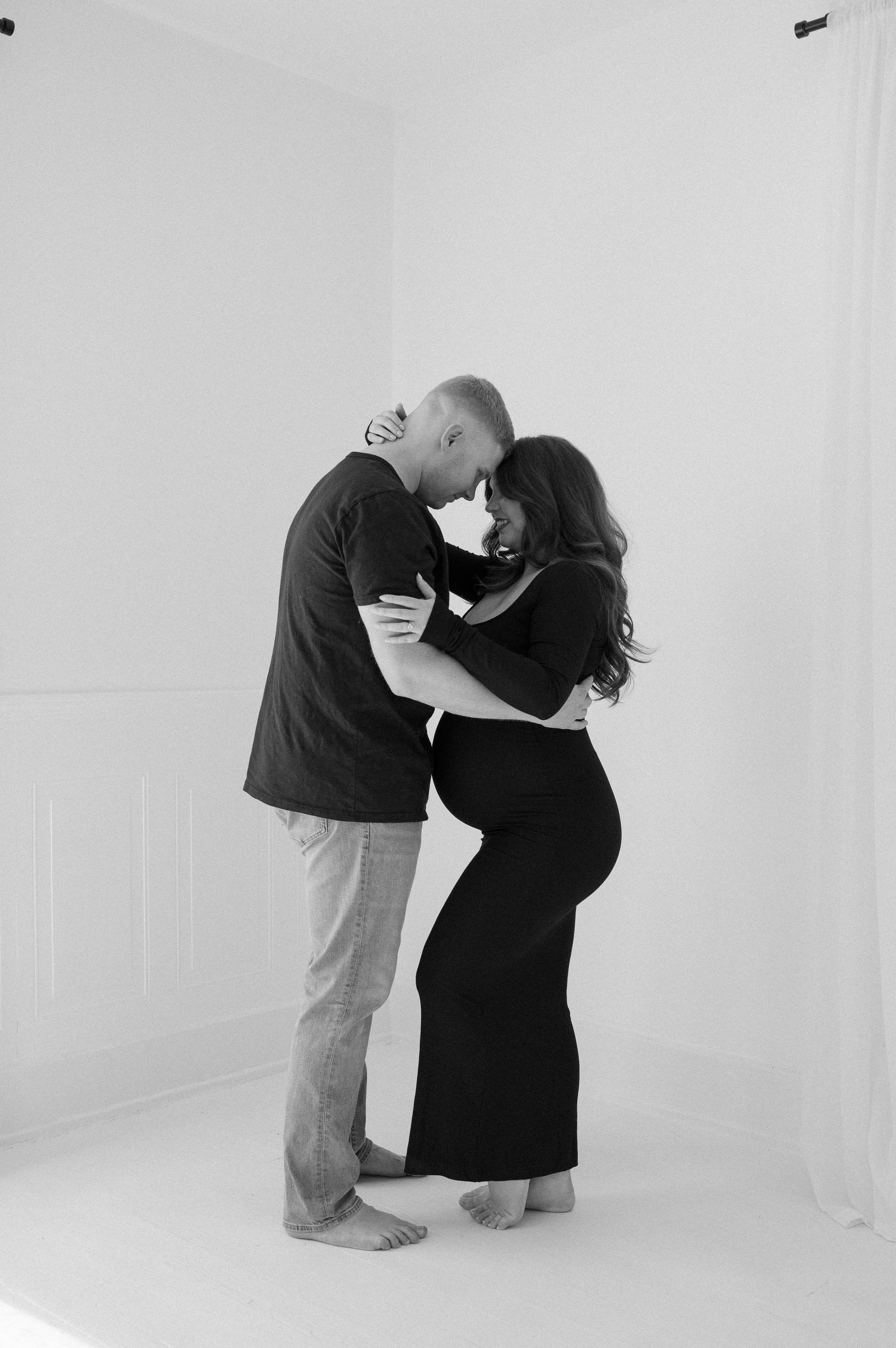 A man and a pregnant woman are hugging each other in a black and white photo.