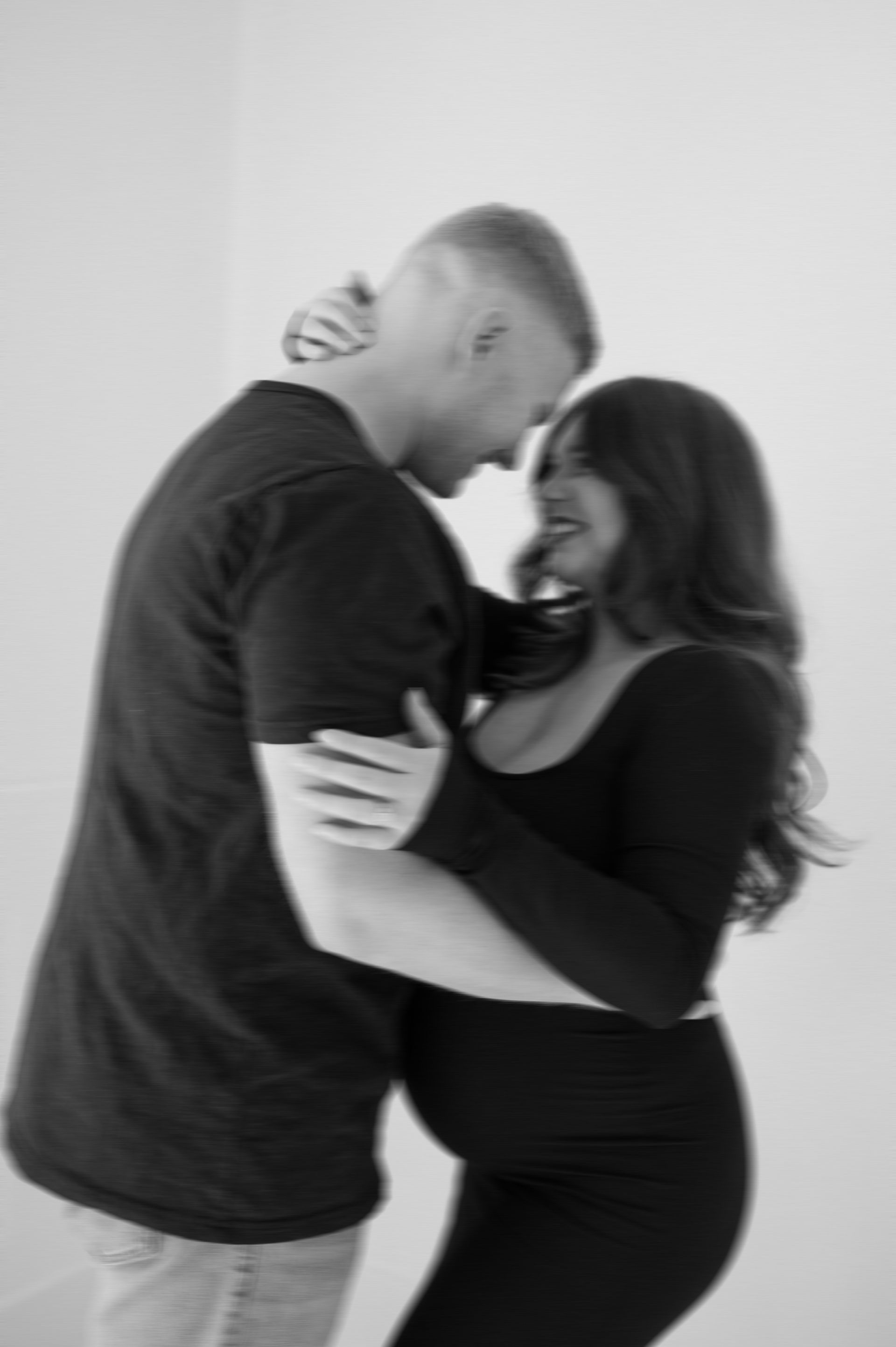 A man and a pregnant woman are hugging each other in a black and white photo.
