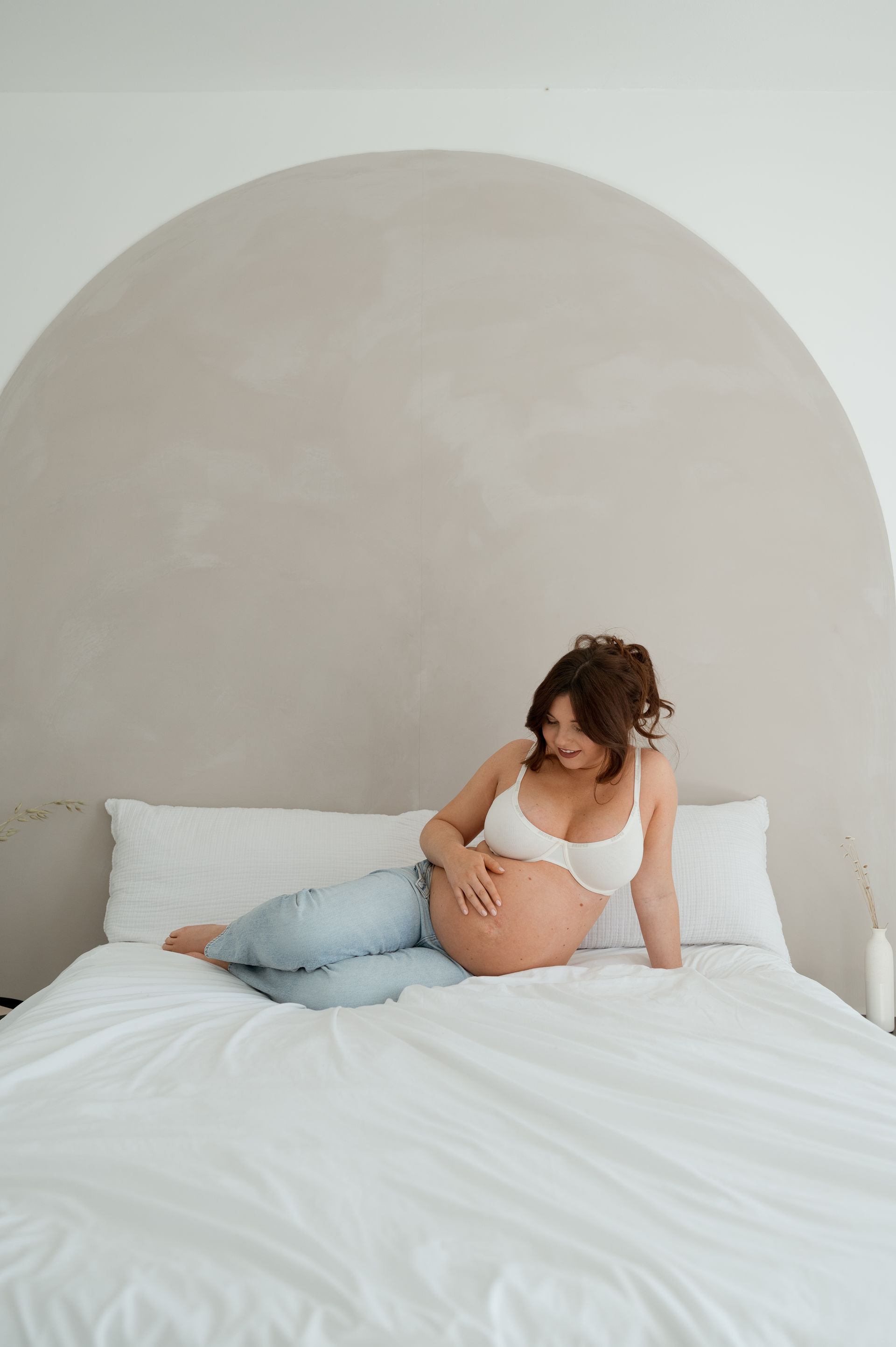 A pregnant woman is sitting on a bed holding her belly.