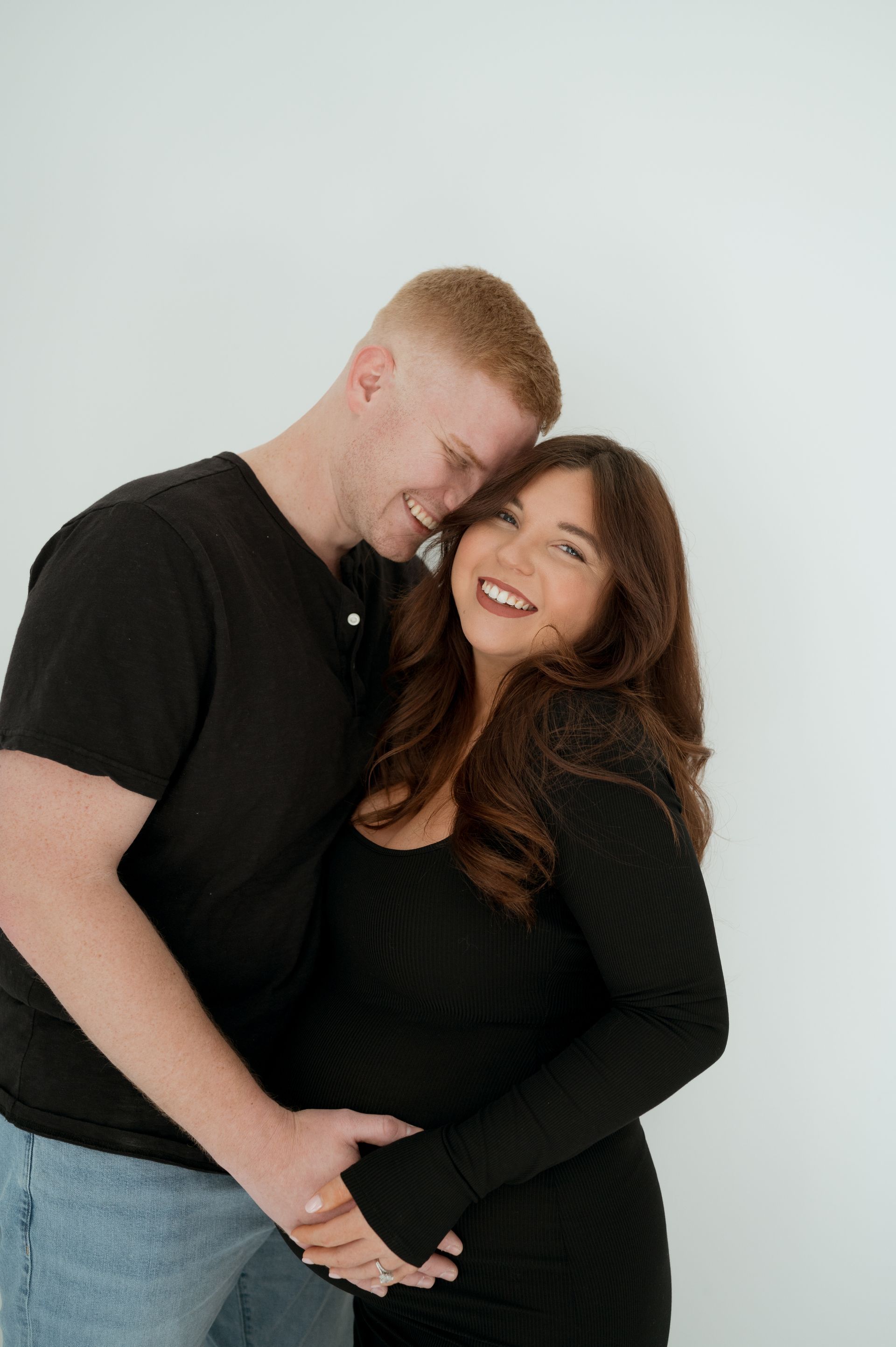 A man is hugging a pregnant woman in a black dress.