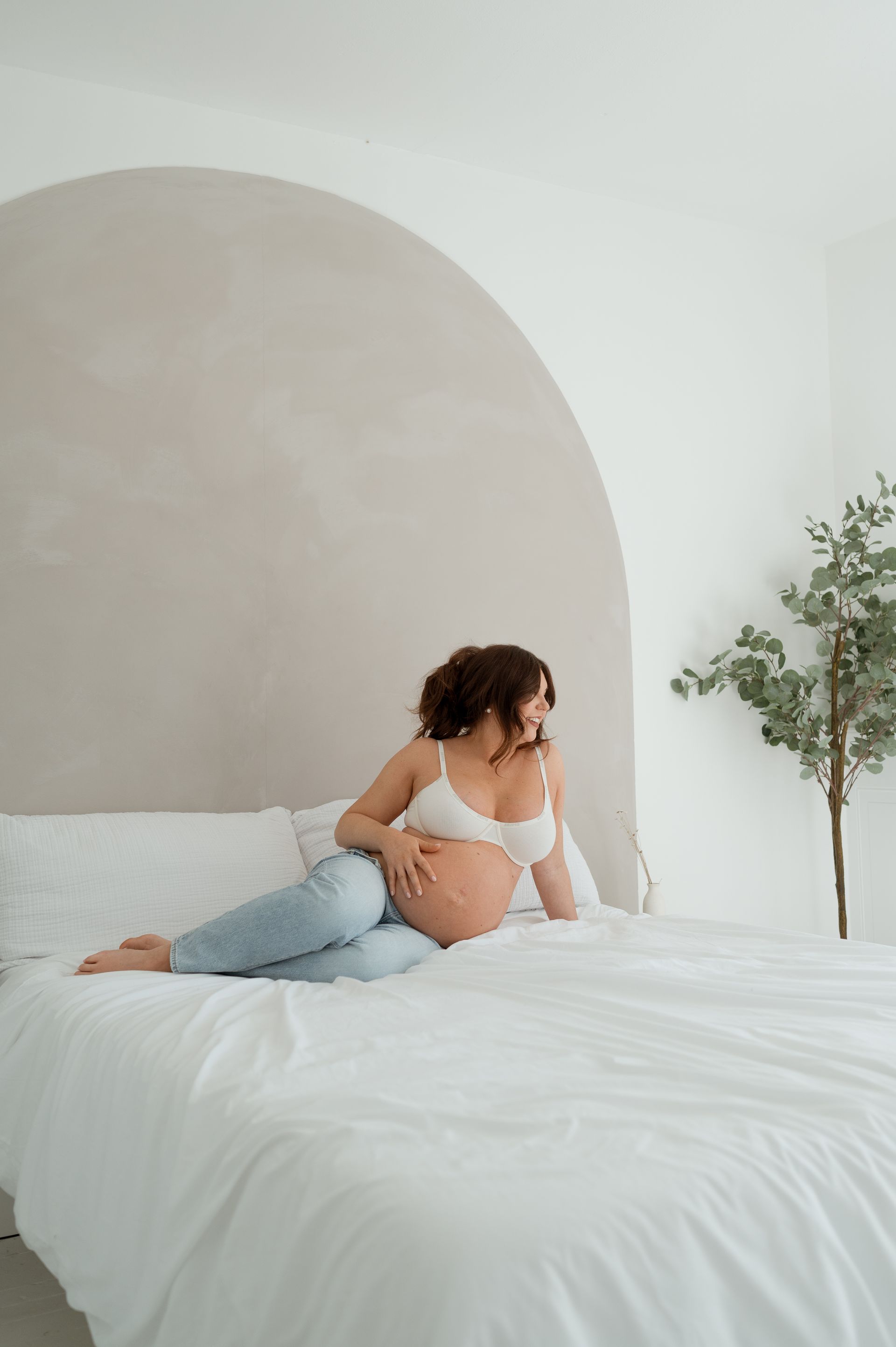 A pregnant woman is sitting on a bed holding her belly.