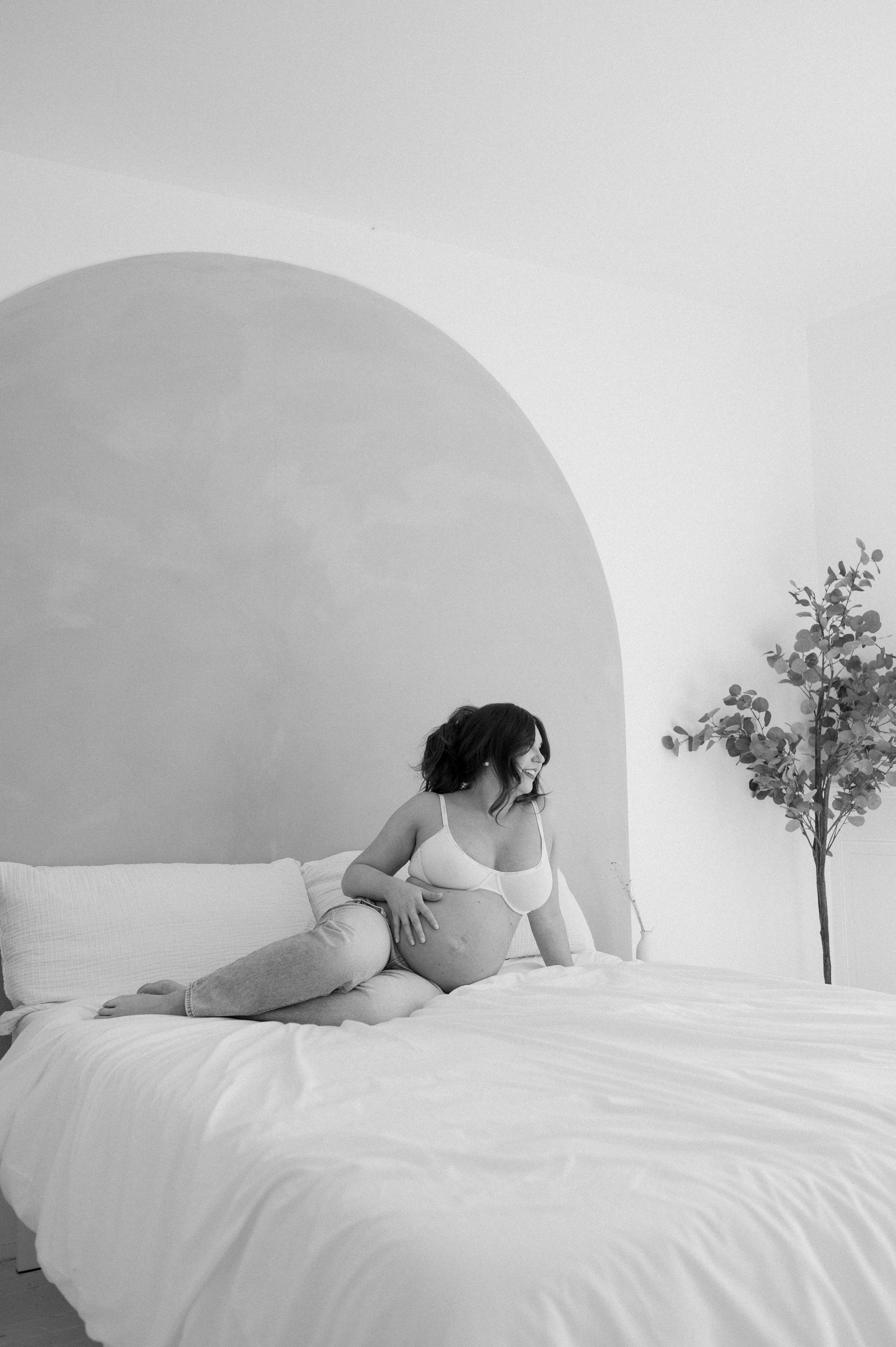 A black and white photo of a pregnant woman laying on a bed.