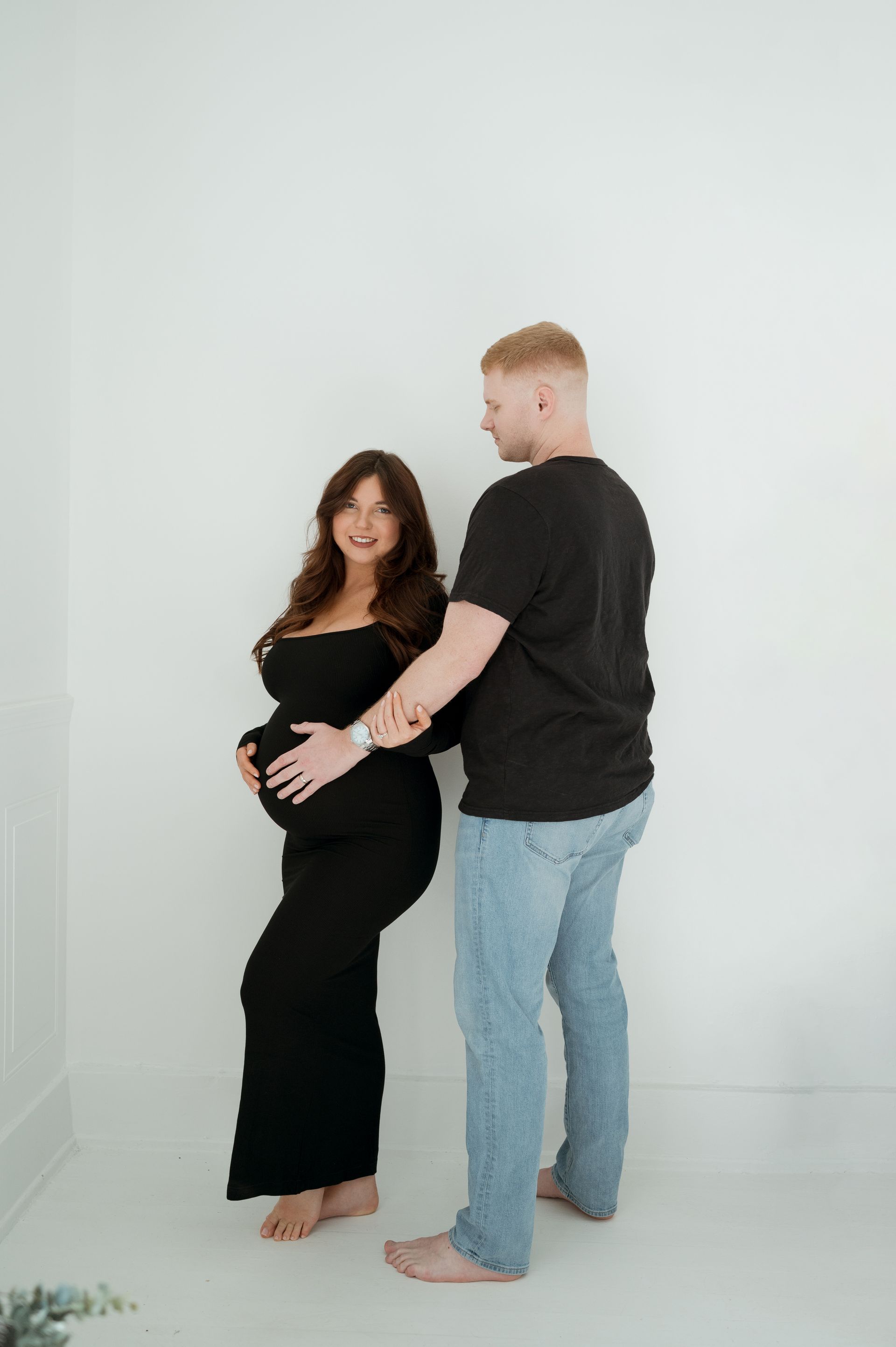A man is standing next to a pregnant woman in a black dress.