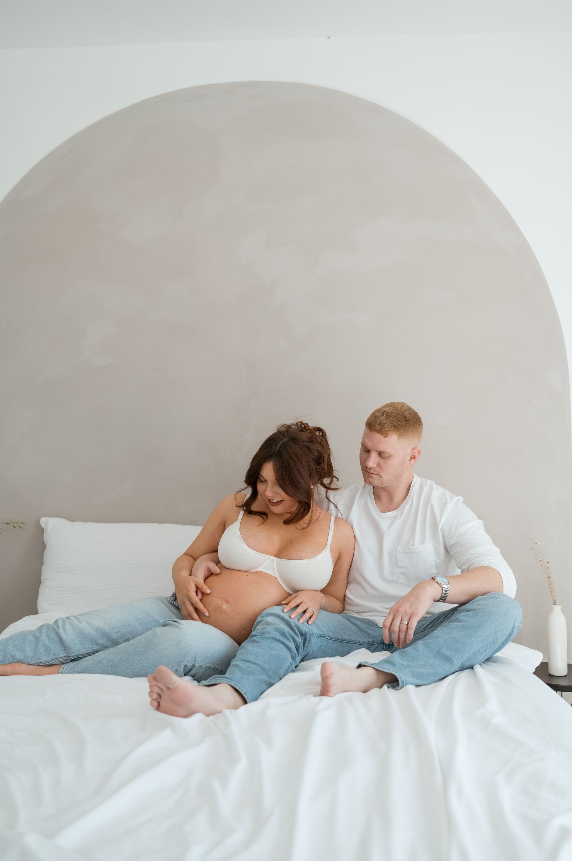 A man and a pregnant woman are sitting on a bed.