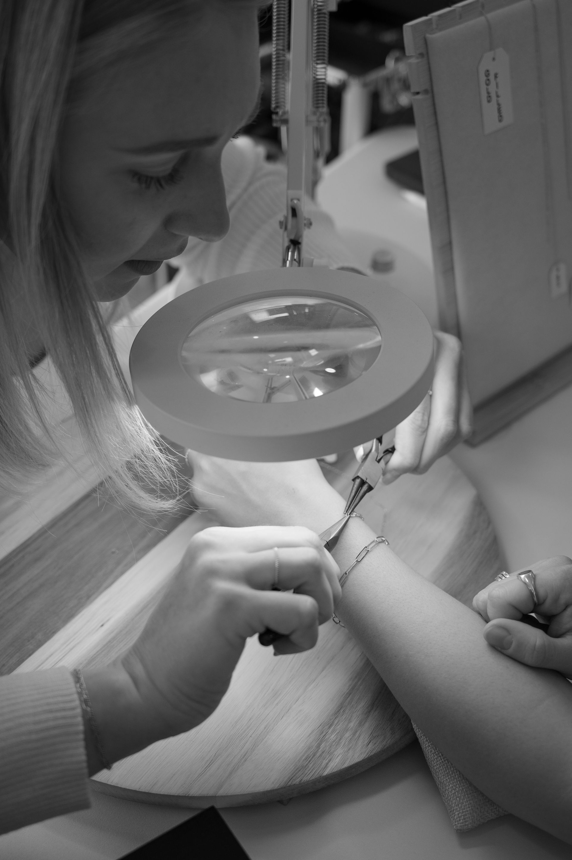 A woman is looking at a bracelet under a magnifying glass