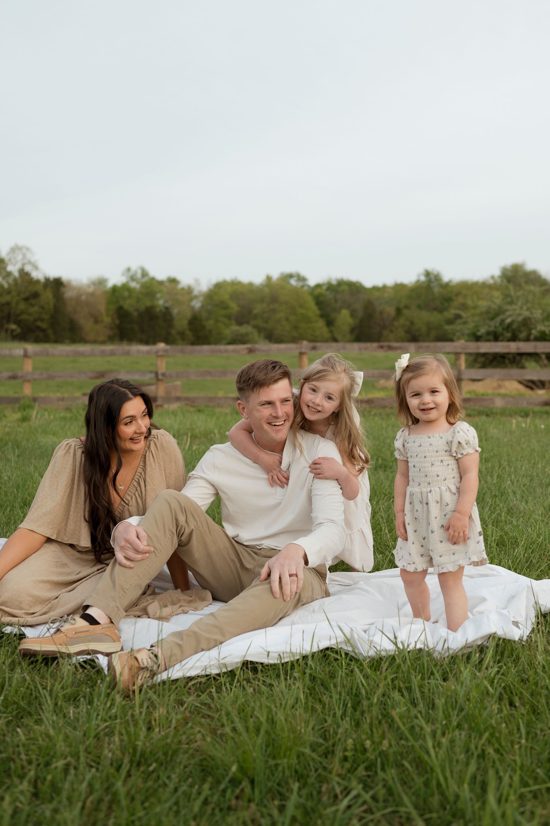 A family is sitting on a blanket in a field.