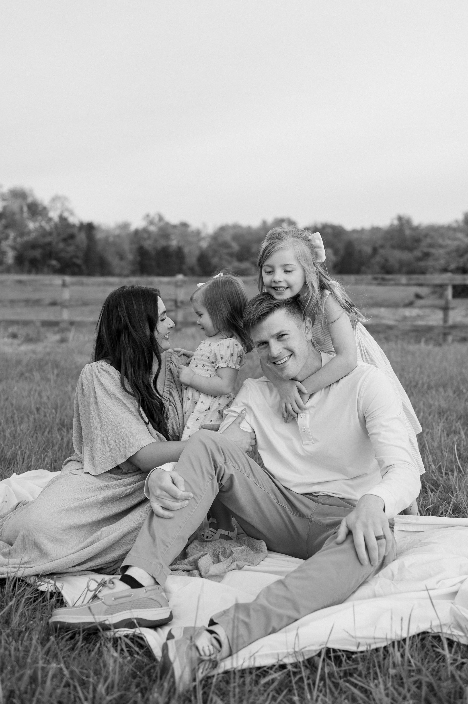 A black and white photo of a family sitting on a blanket in a field.