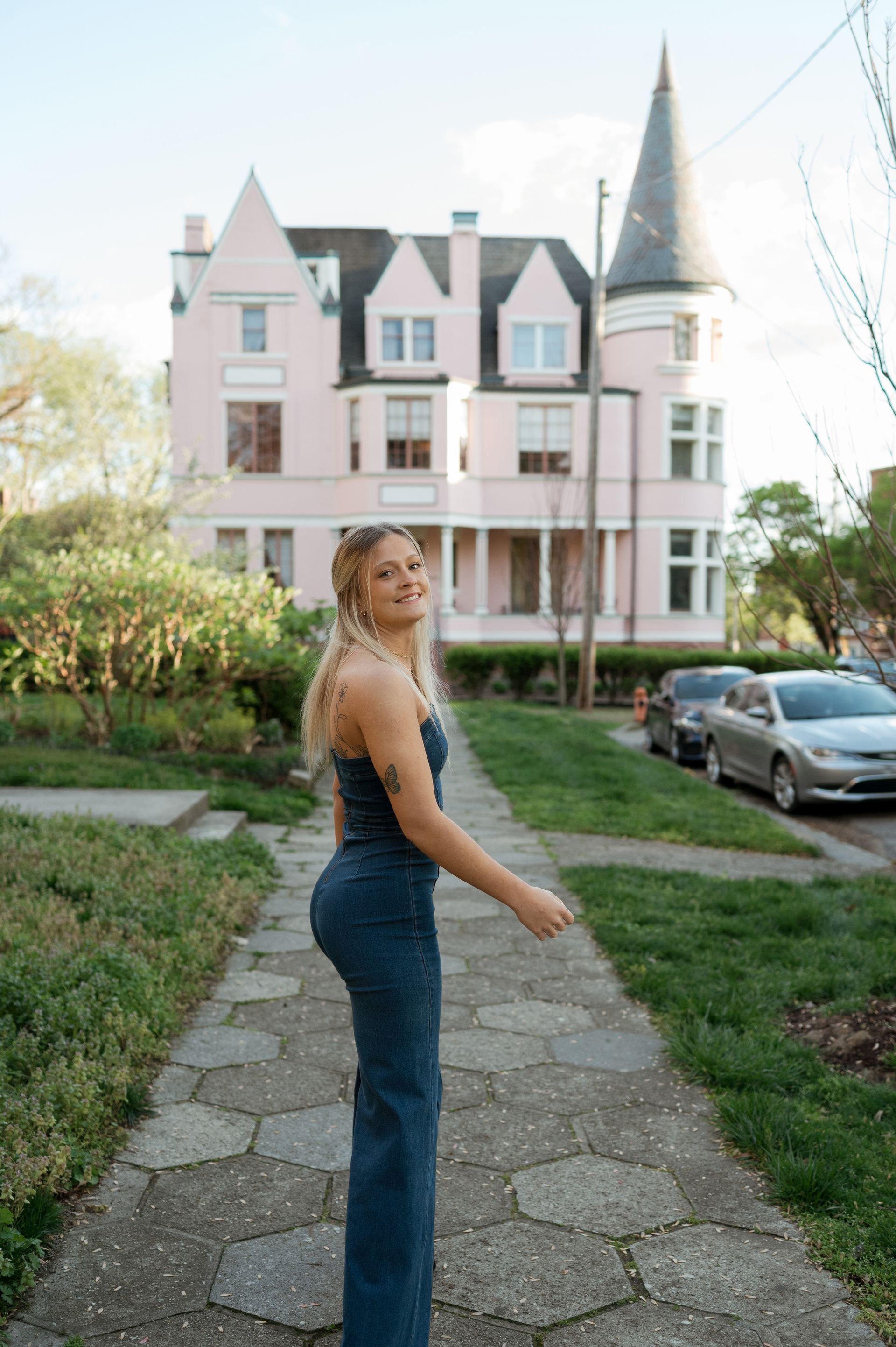 A woman in a blue dress is standing on a sidewalk in front of a pink house.