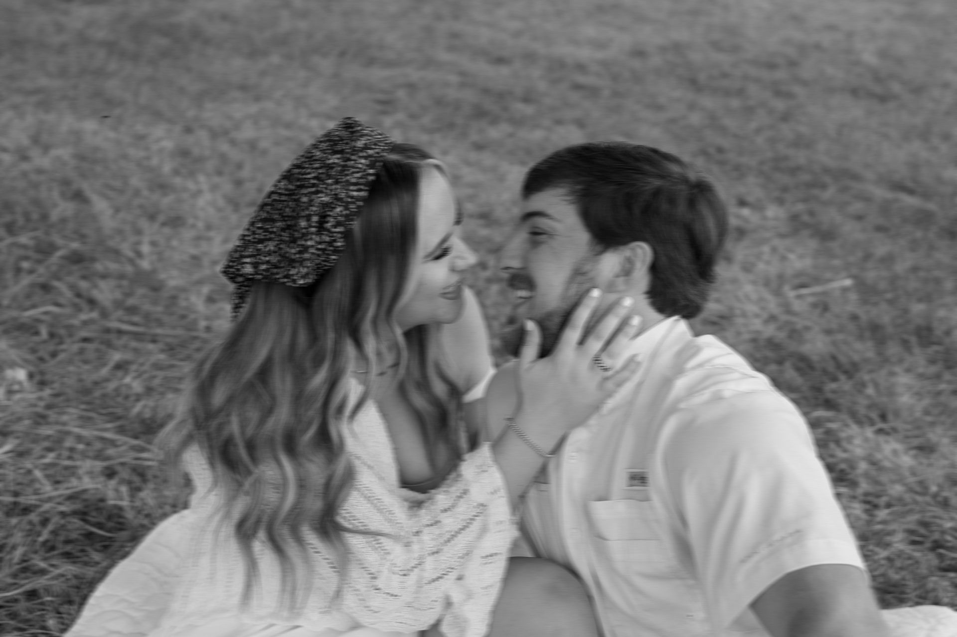 A black and white photo of a man and woman kissing in a field.