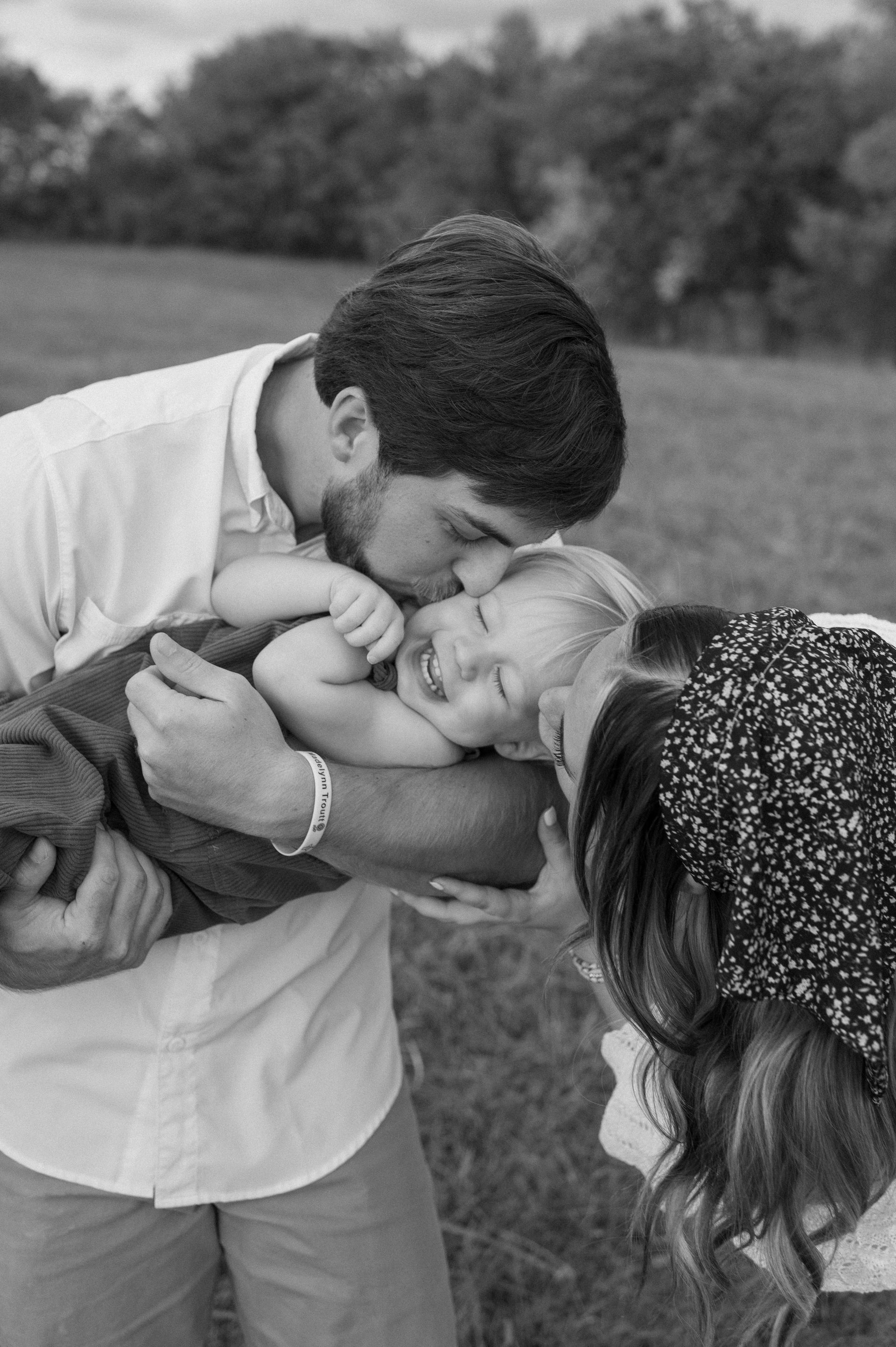 A man is kissing a baby on the forehead while a woman holds a baby.