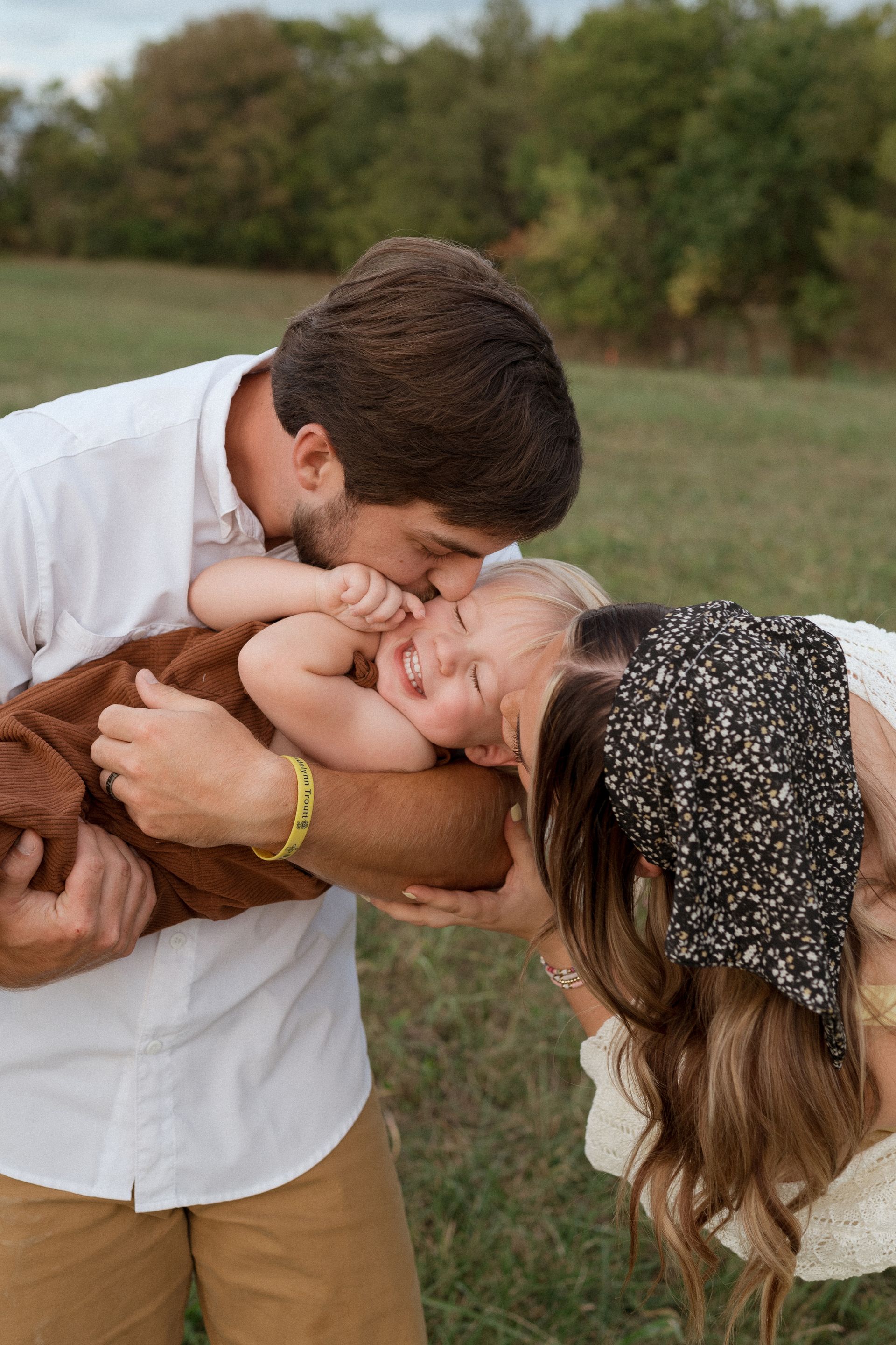 A man is kissing a baby on the cheek in a field.