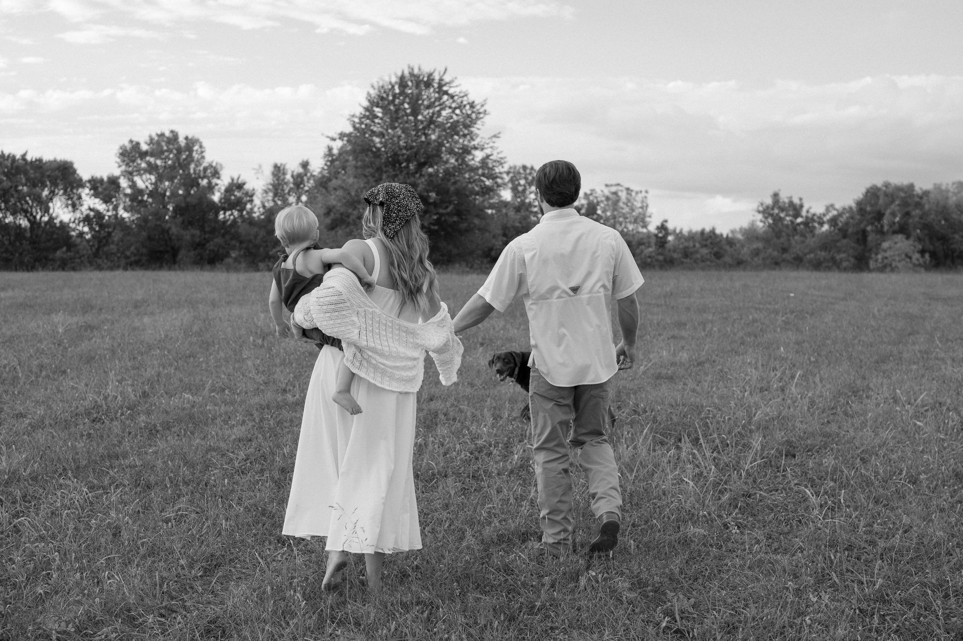 A black and white photo of a family walking through a grassy field.