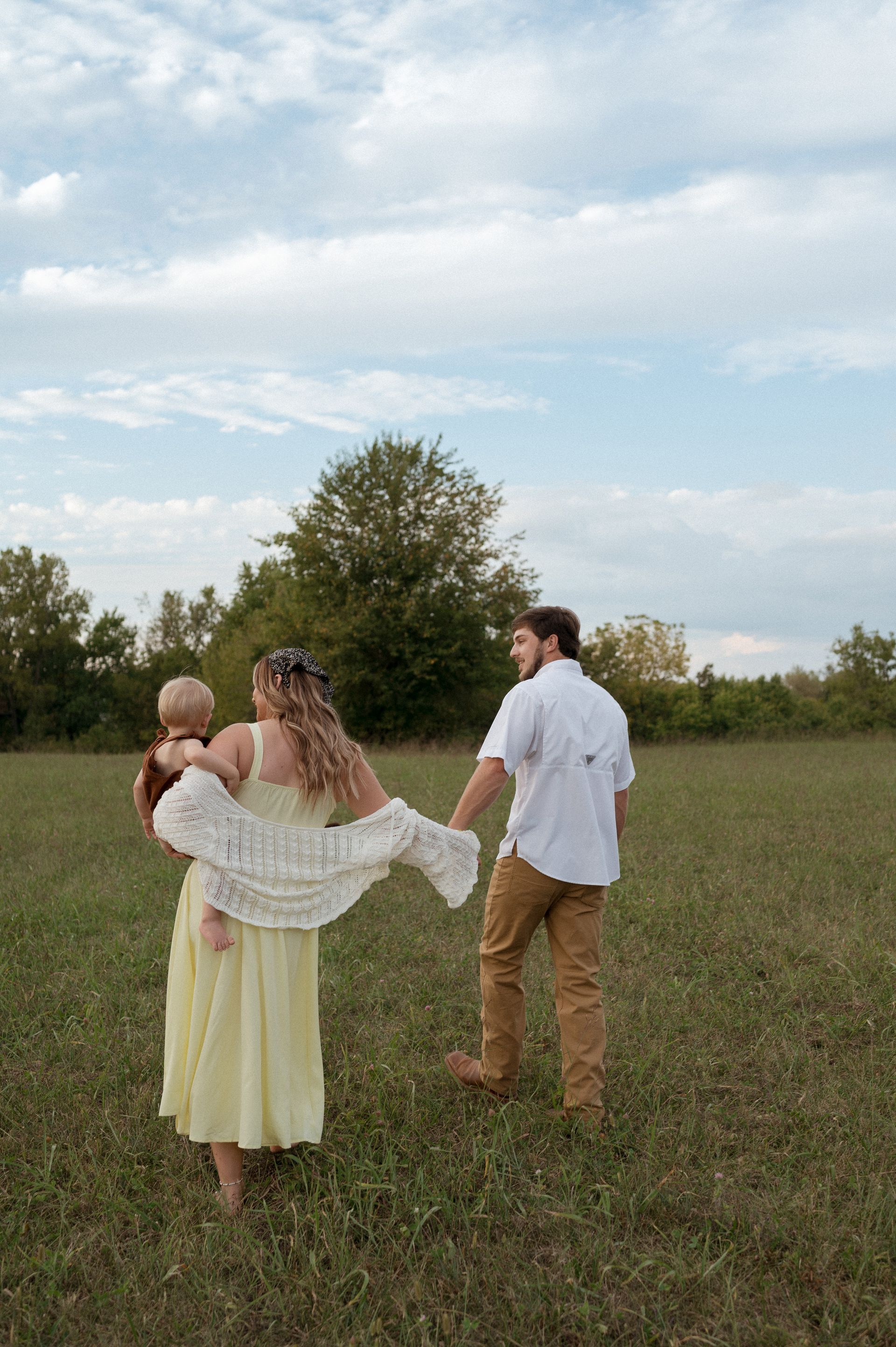 A man and a woman are holding a baby in a field.