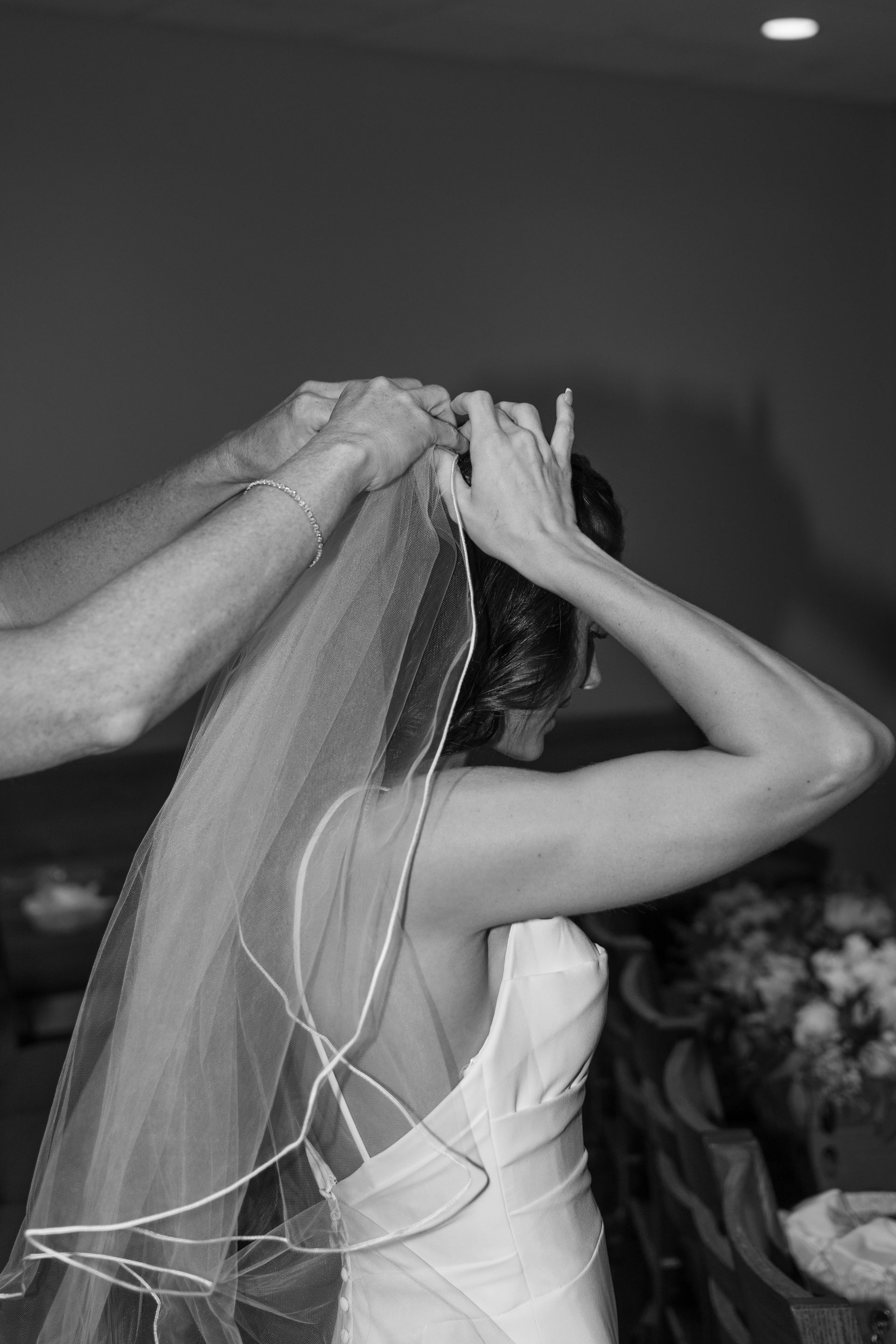A black and white photo of a bride putting on her veil.