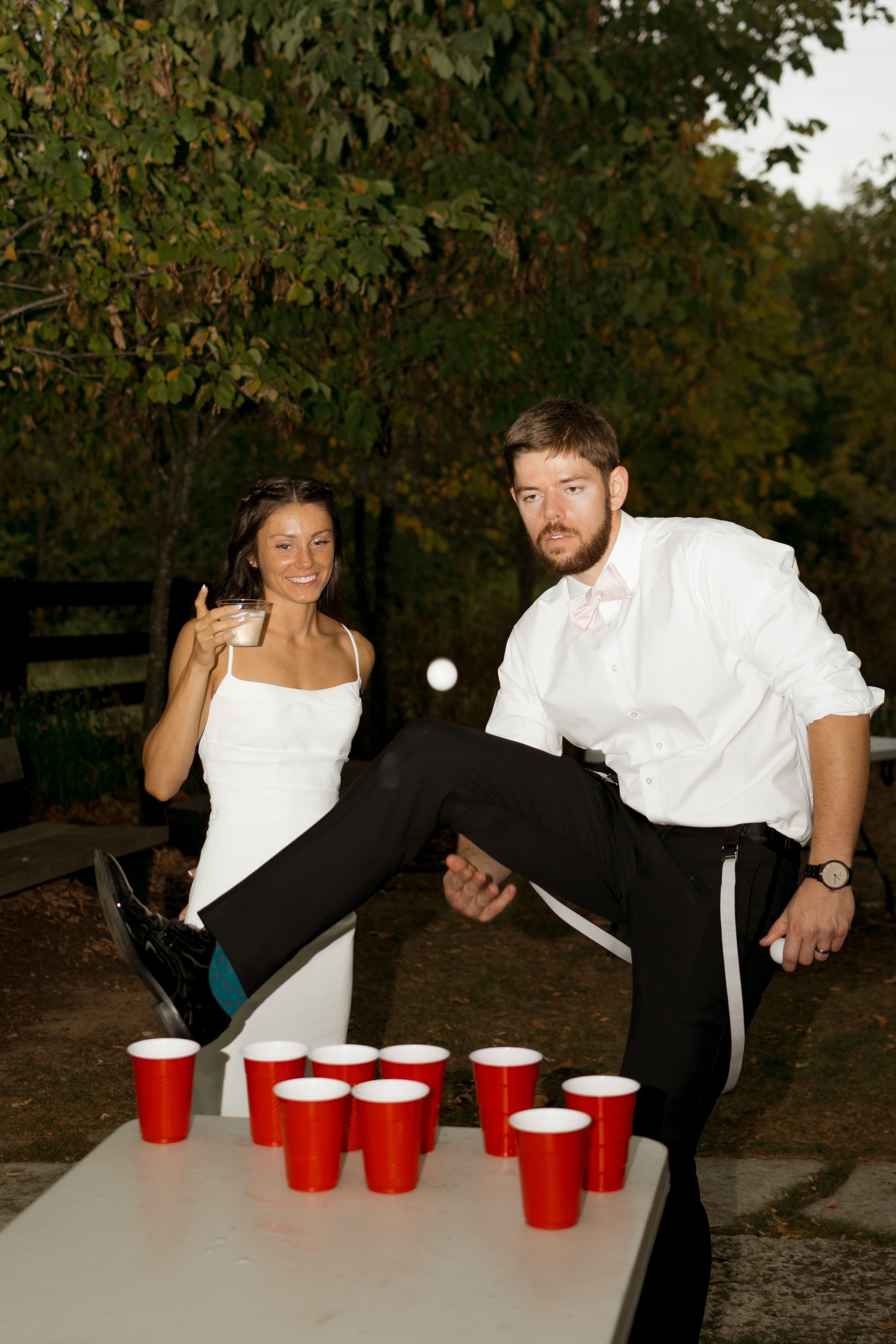 A bride and groom are playing beer pong with red cups