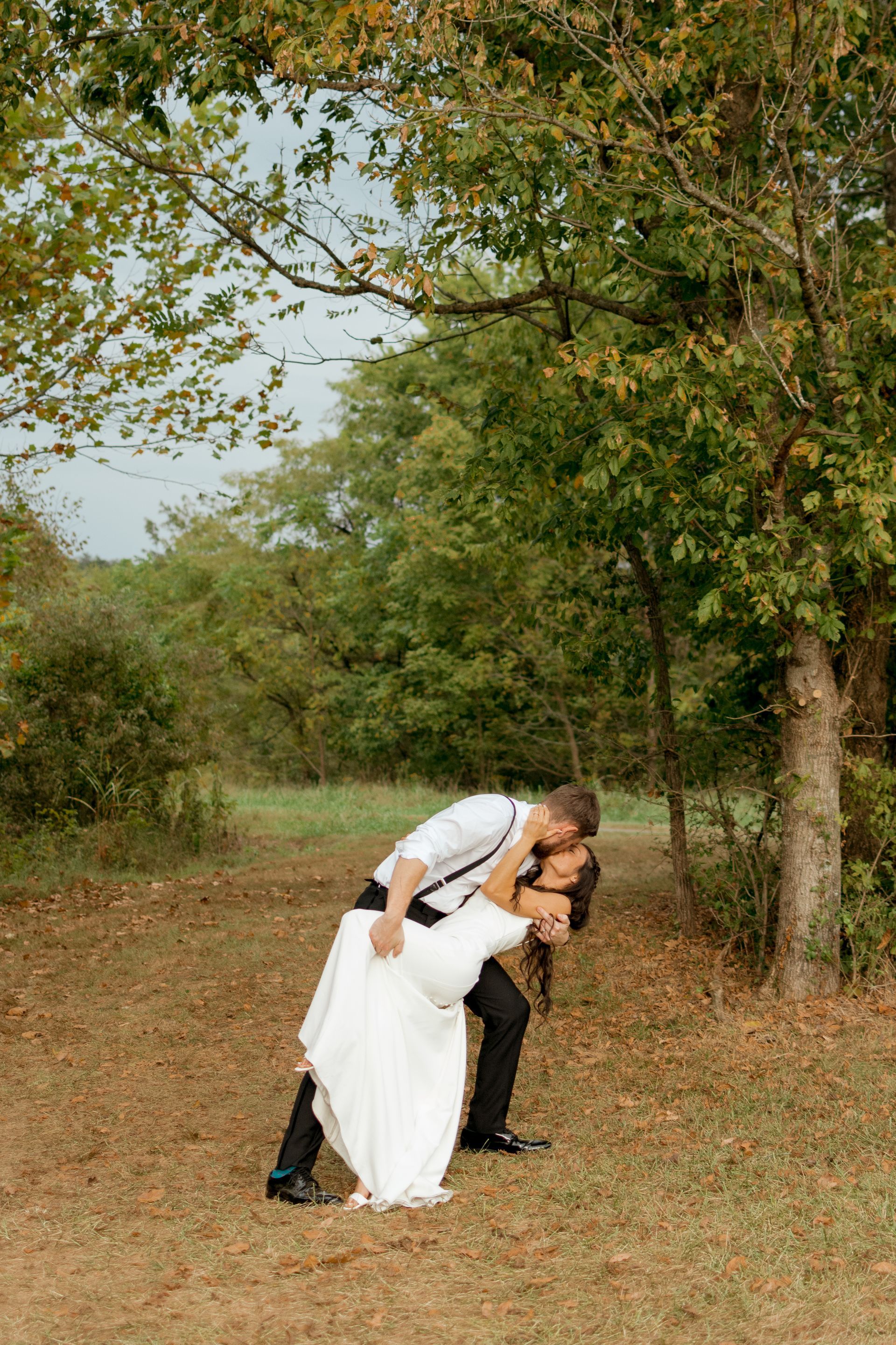 A bride and groom are kissing under a tree in a field.