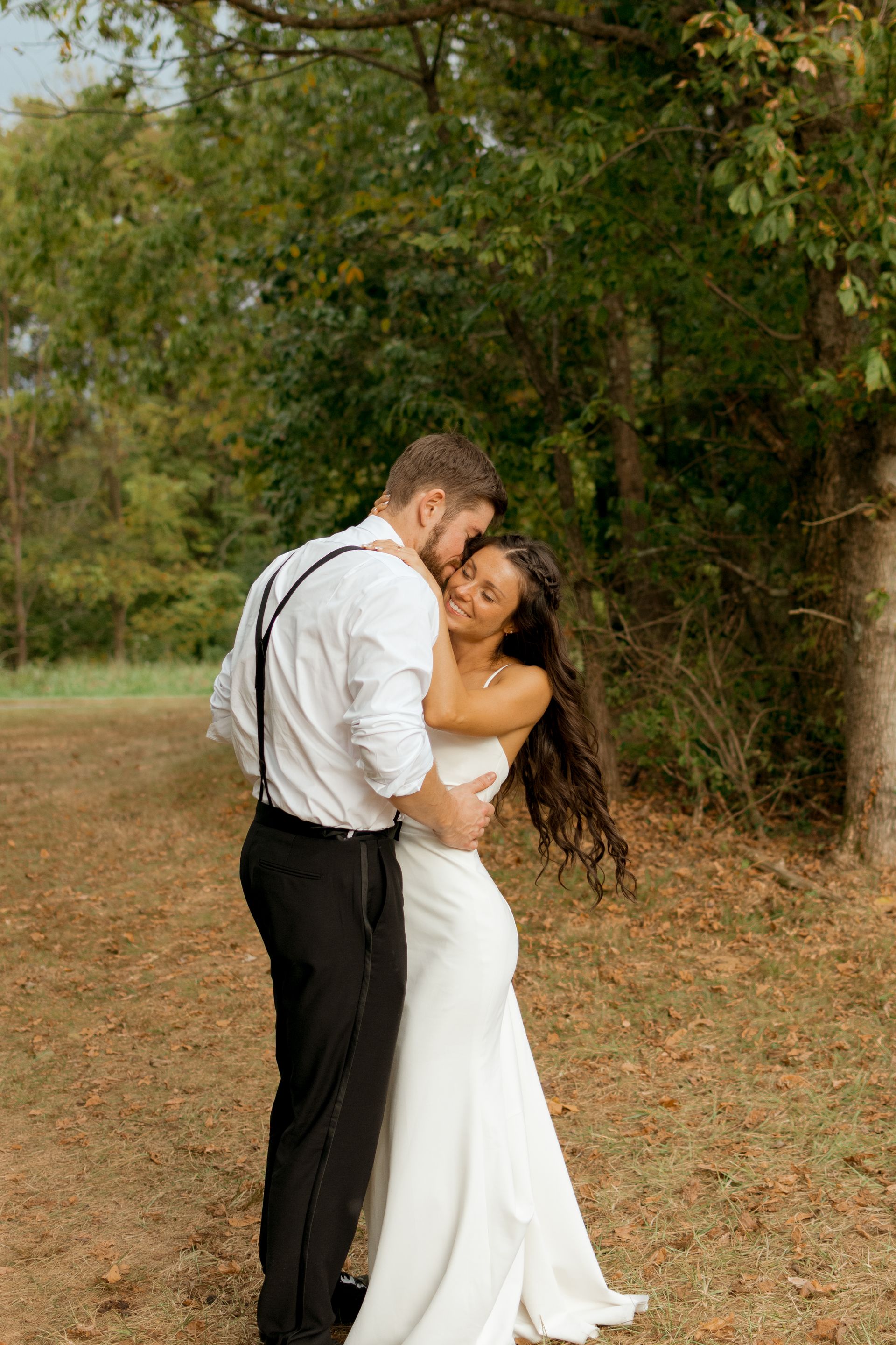 A bride and groom are hugging each other in a field.