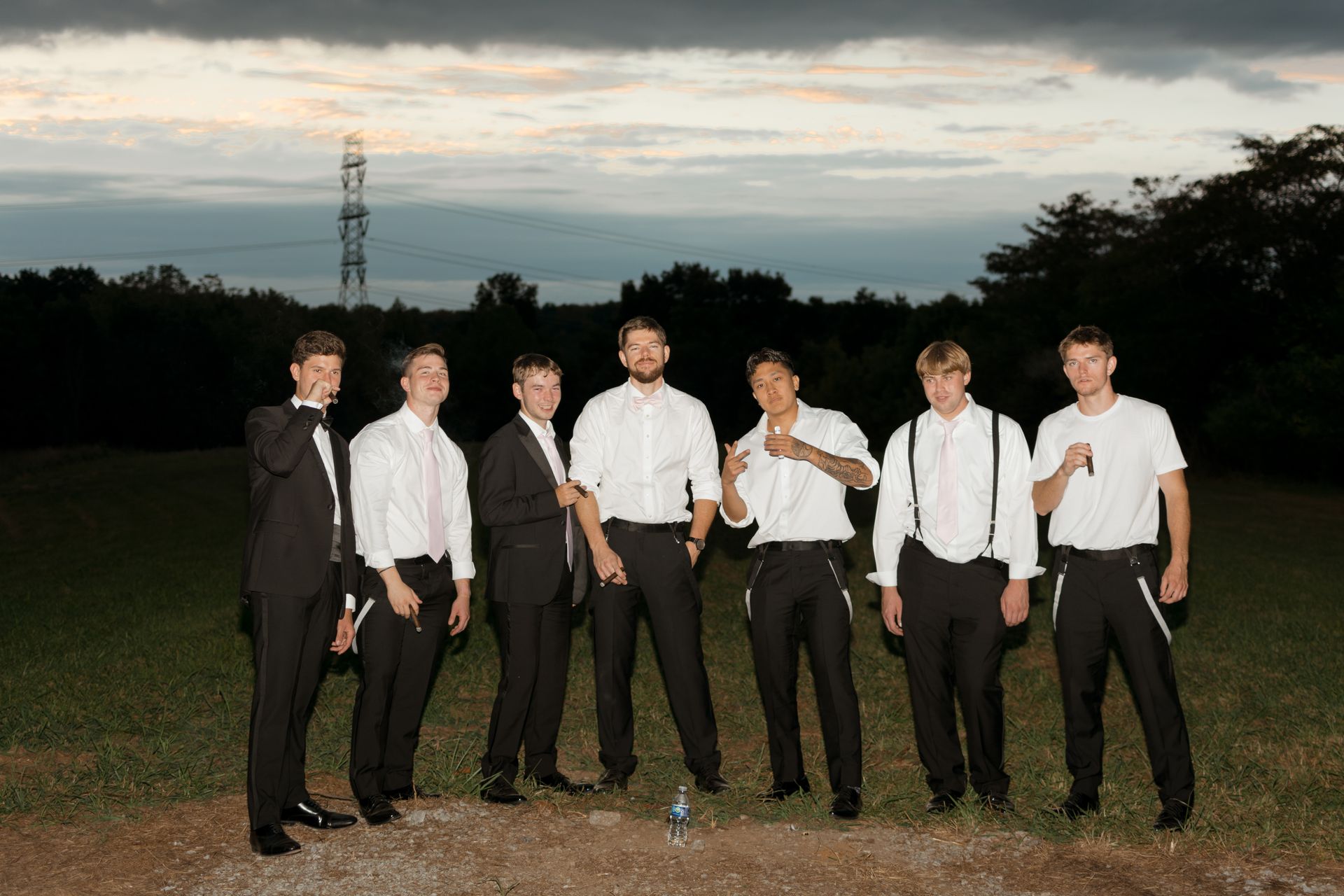 A group of men in suits and white shirts are standing in a field.