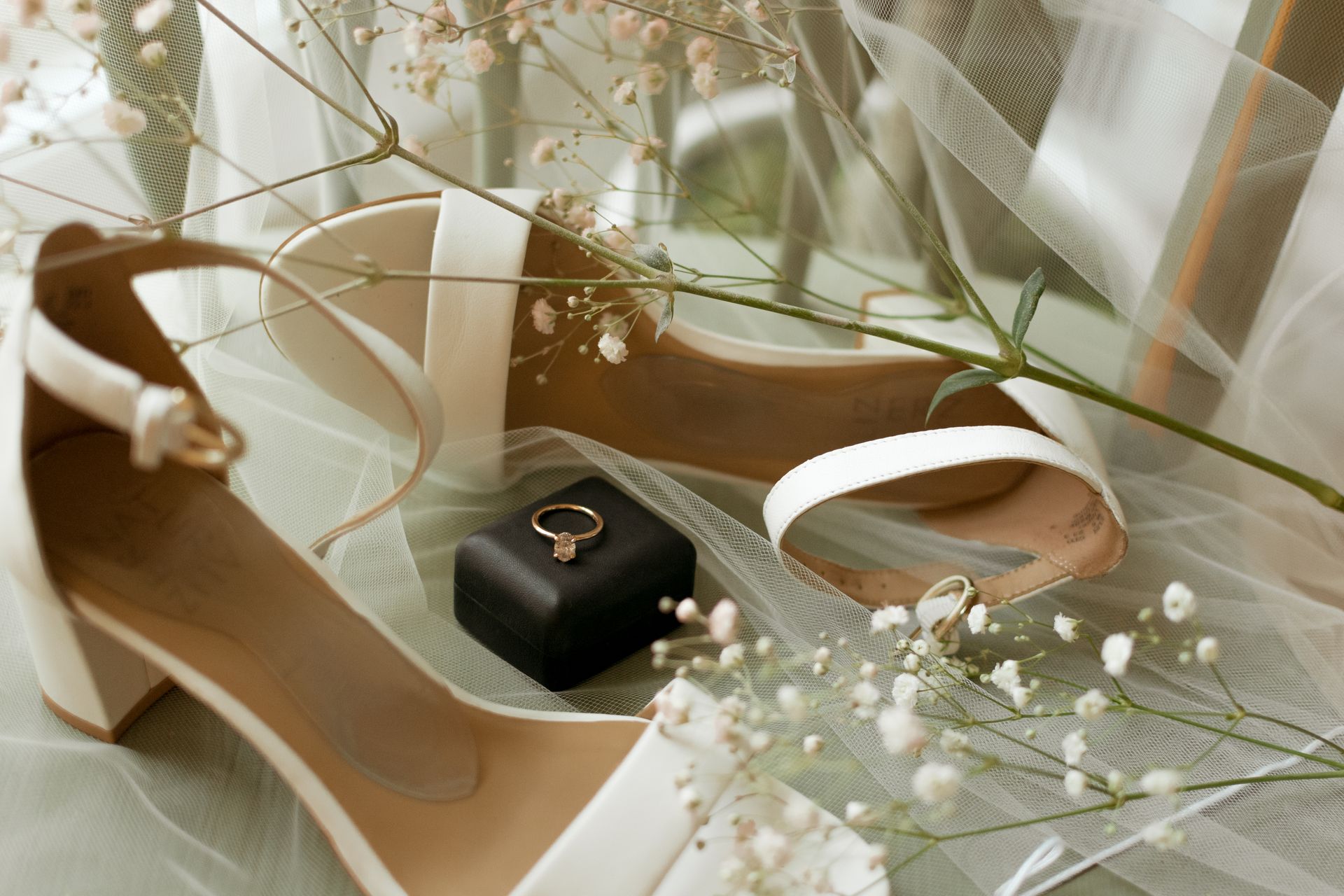 A pair of white shoes with a ring in a box on top of them.