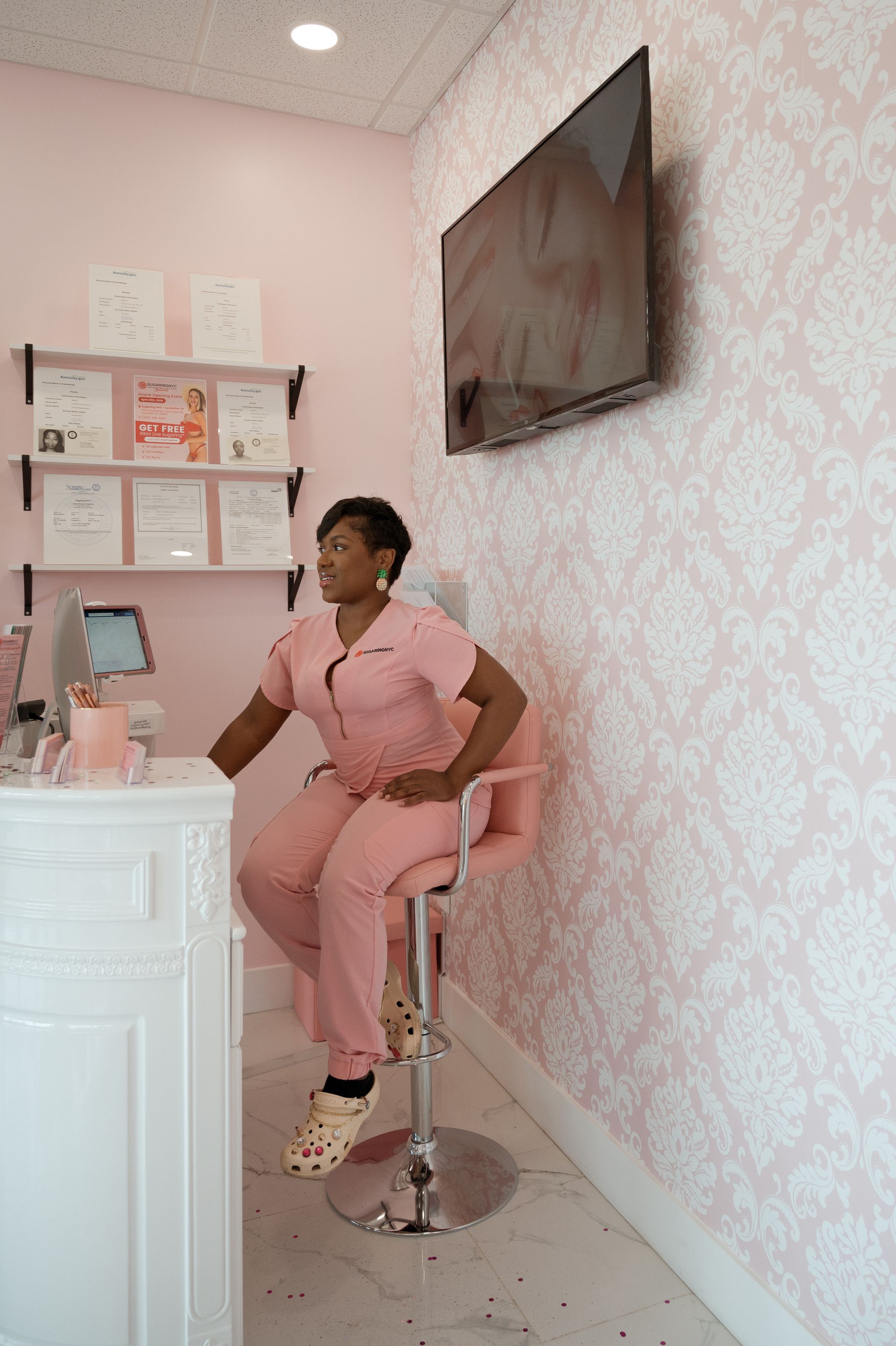 A woman in pink scrubs is sitting on a chair in a pink room.