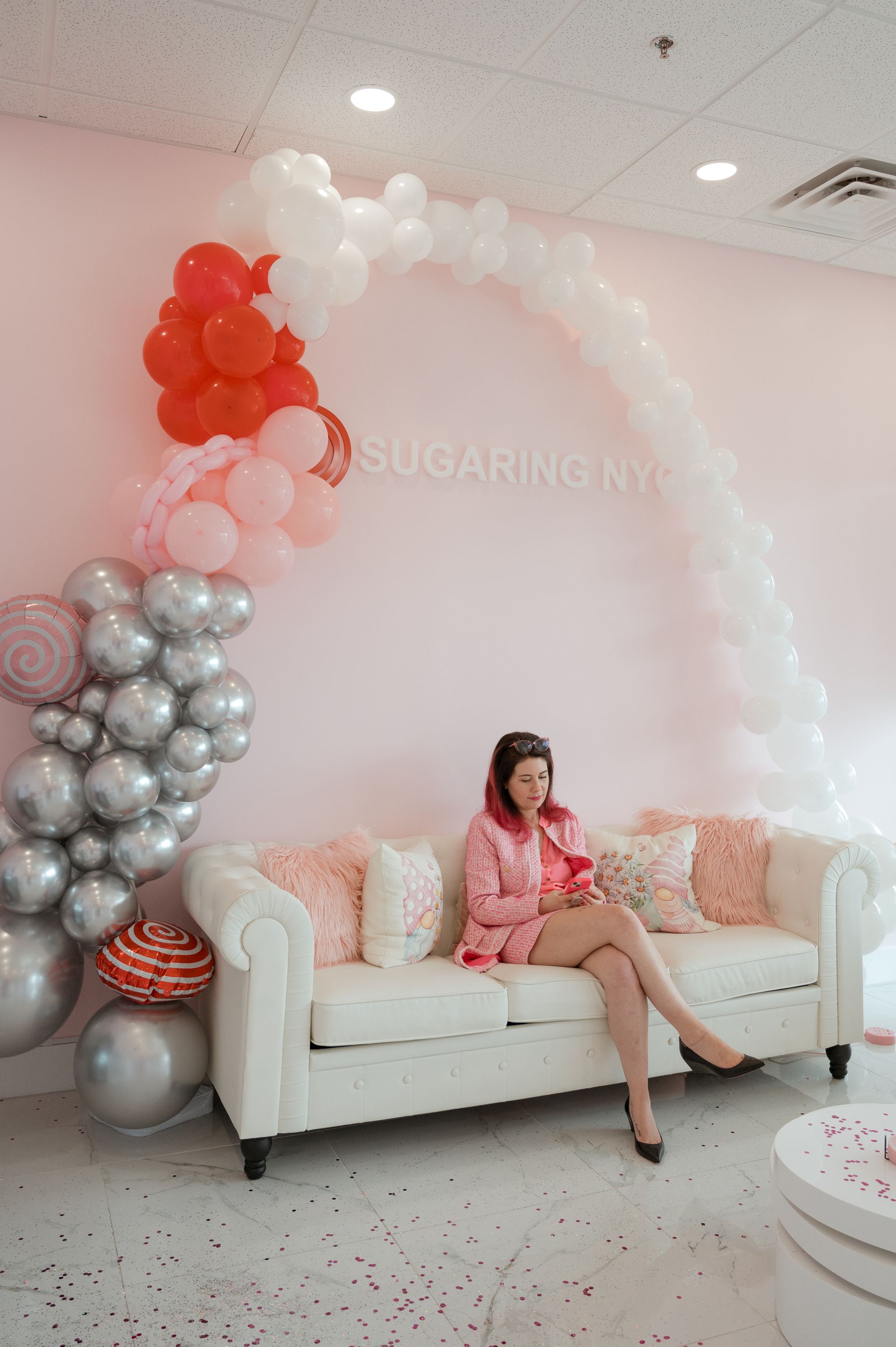 A woman is sitting on a couch in front of a balloon arch.