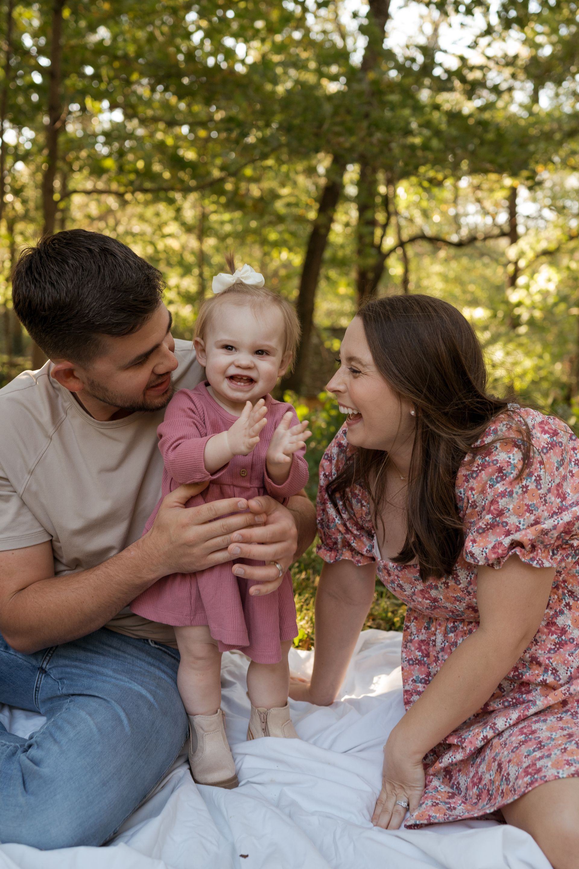 A man and woman are sitting on a blanket holding a baby girl.