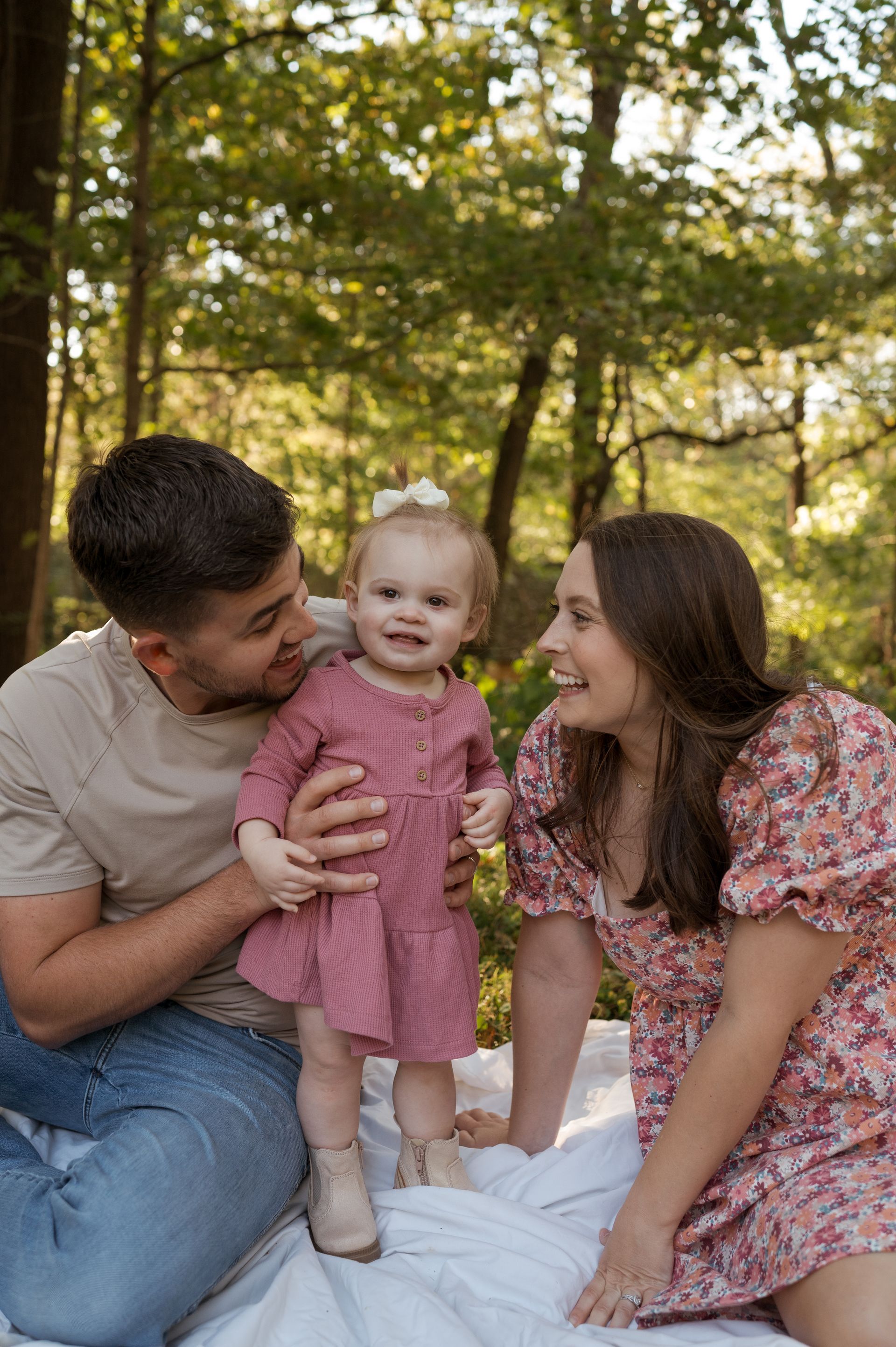 A man and woman are sitting on a blanket holding a baby girl.