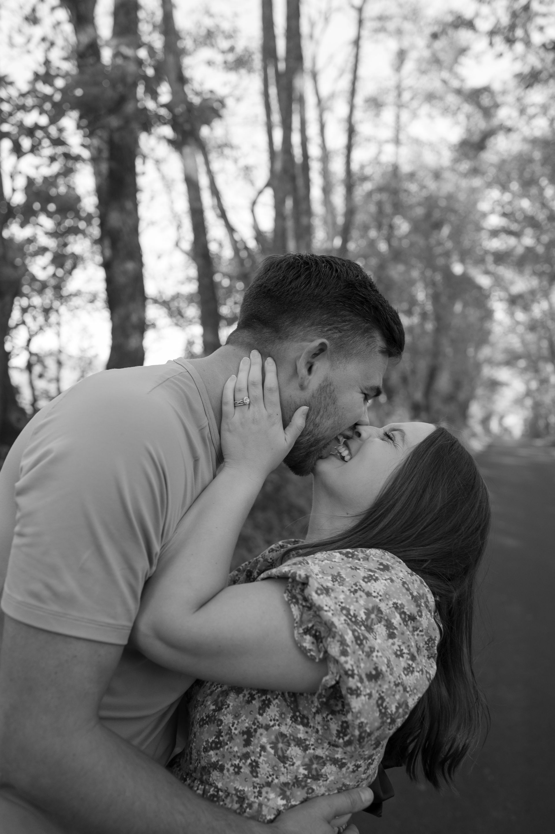 A black and white photo of a man and woman kissing in the woods.