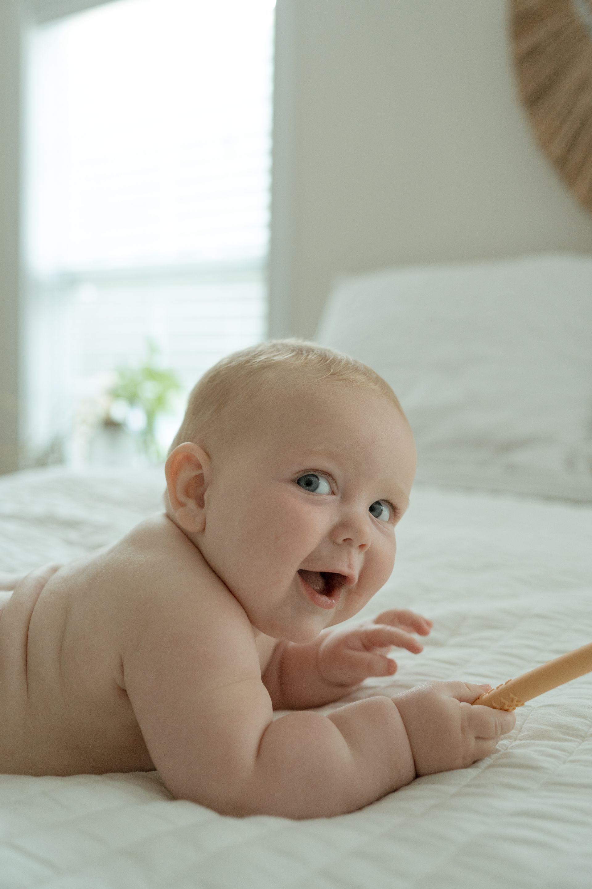 A baby is laying on its stomach on a bed and smiling.