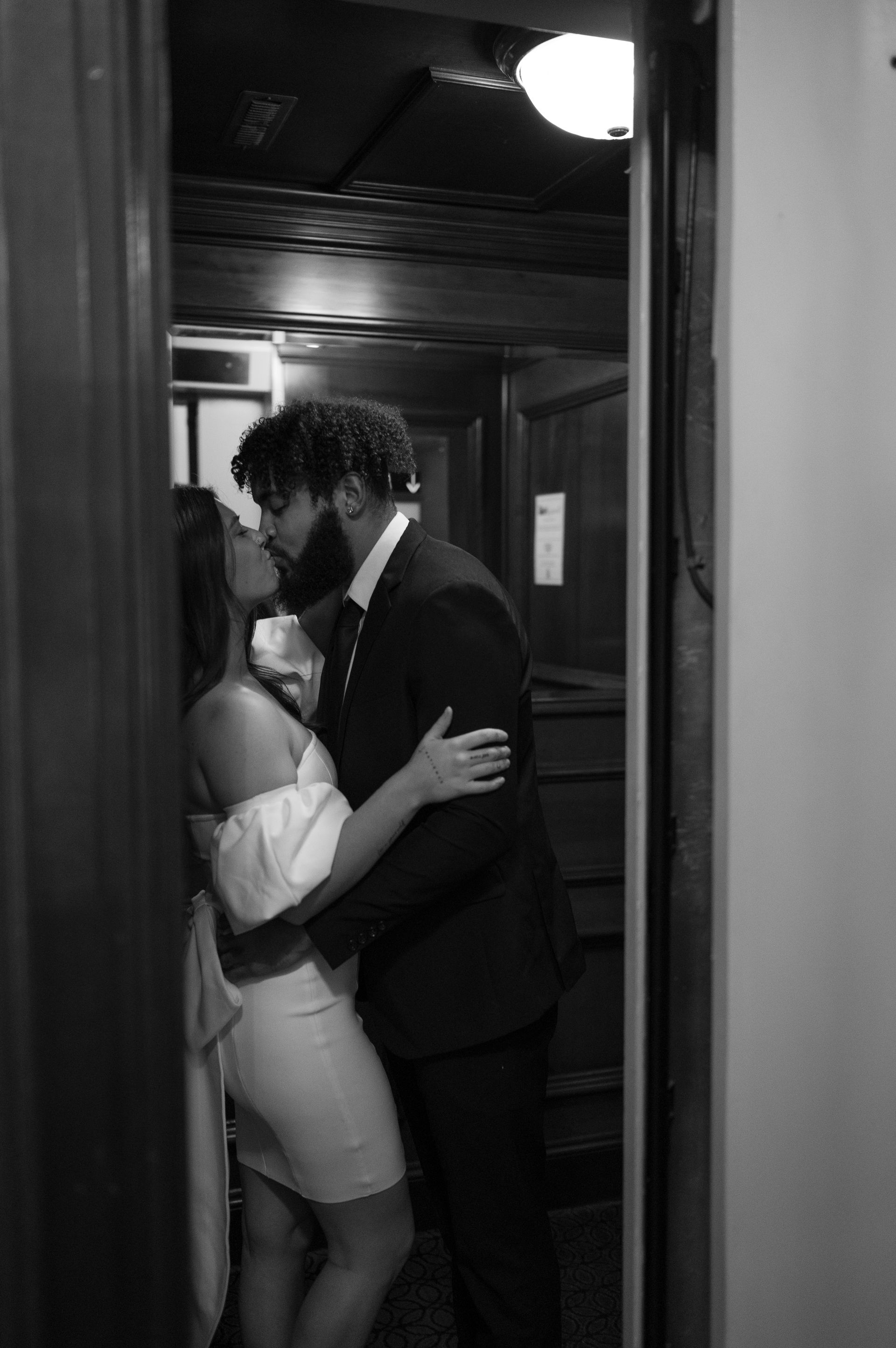 A black and white photo of a man and woman kissing in a doorway.
