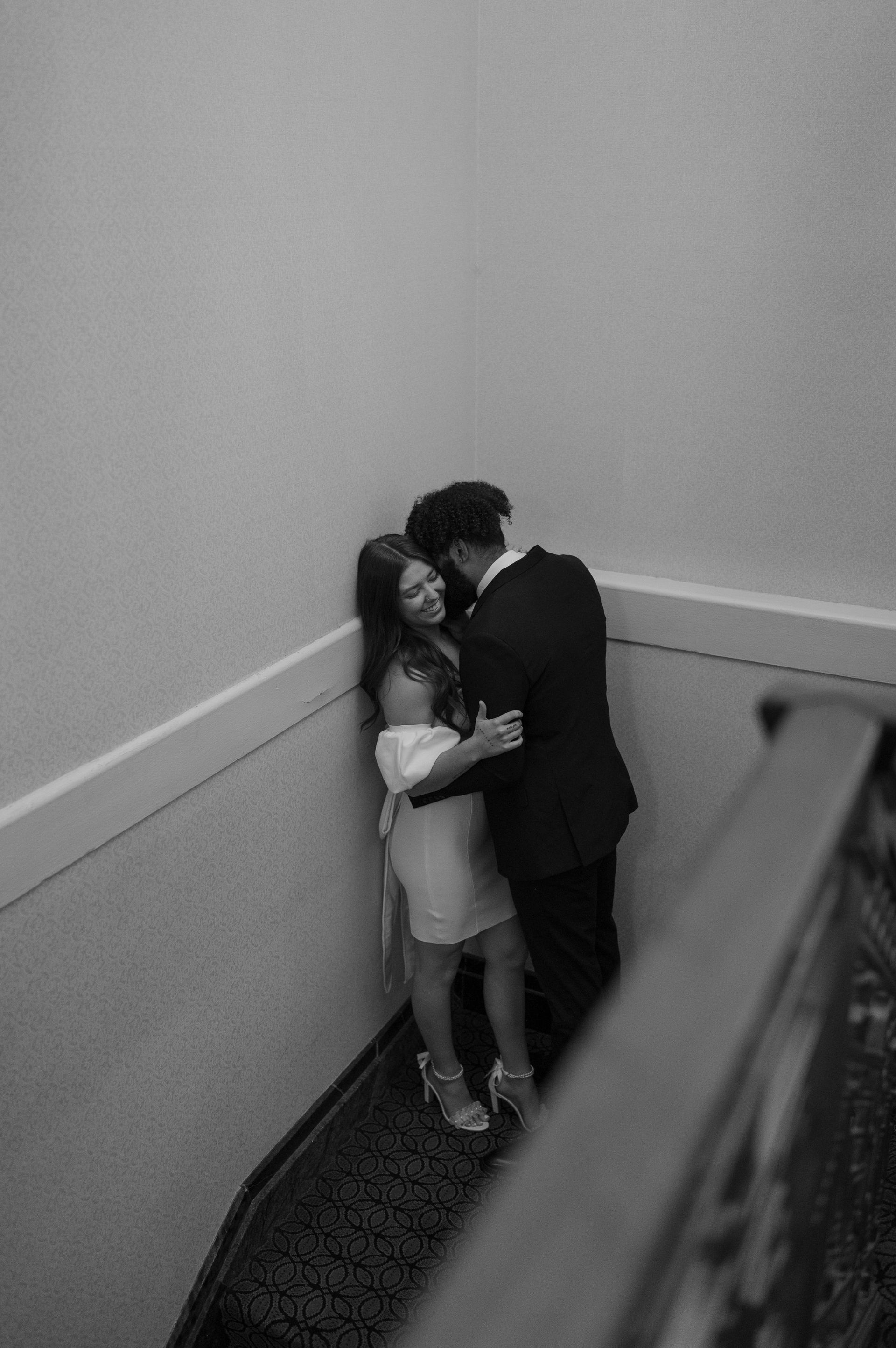 A black and white photo of a bride and groom hugging on a set of stairs.