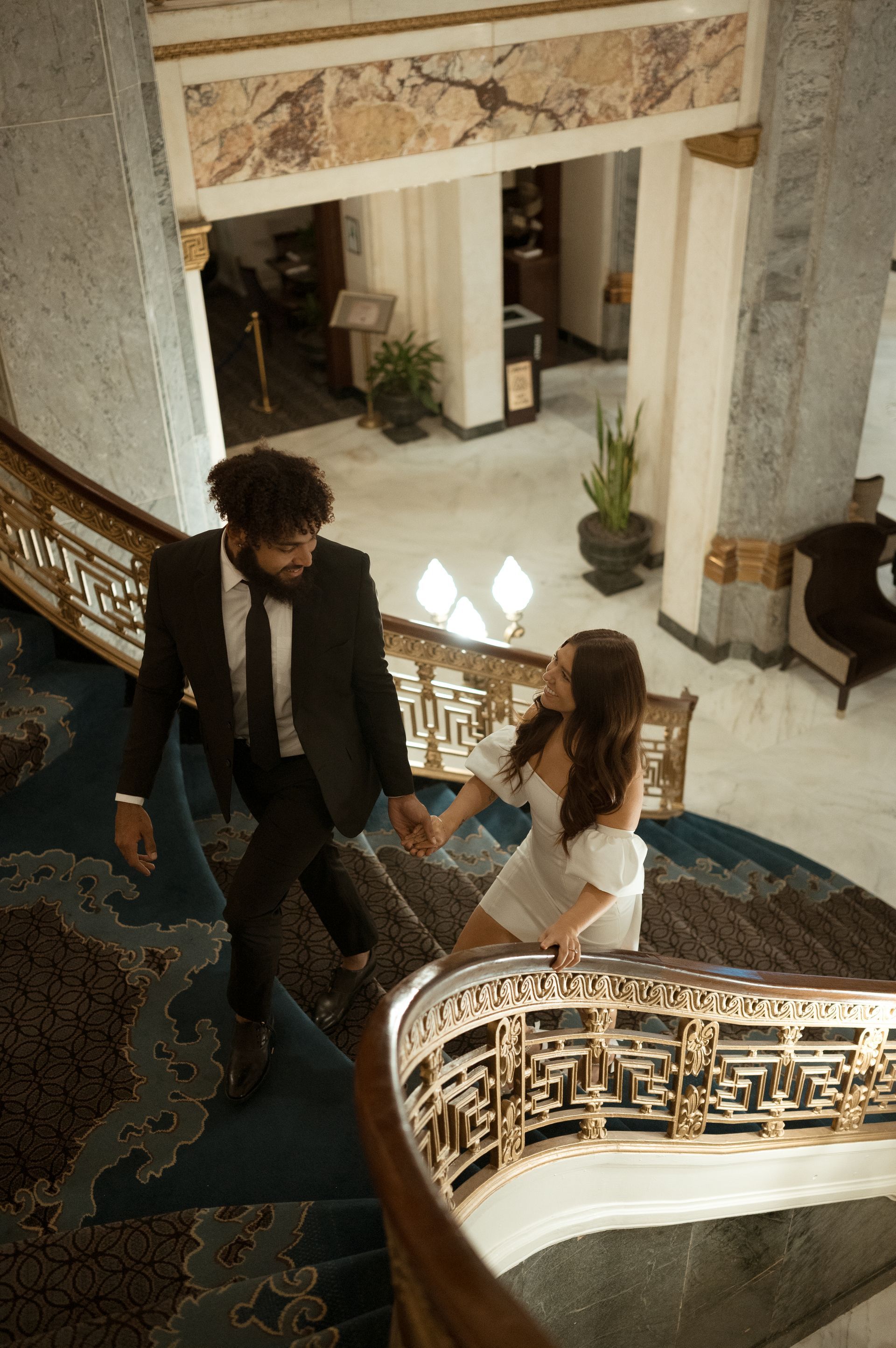 A bride and groom are walking down a spiral staircase holding hands.