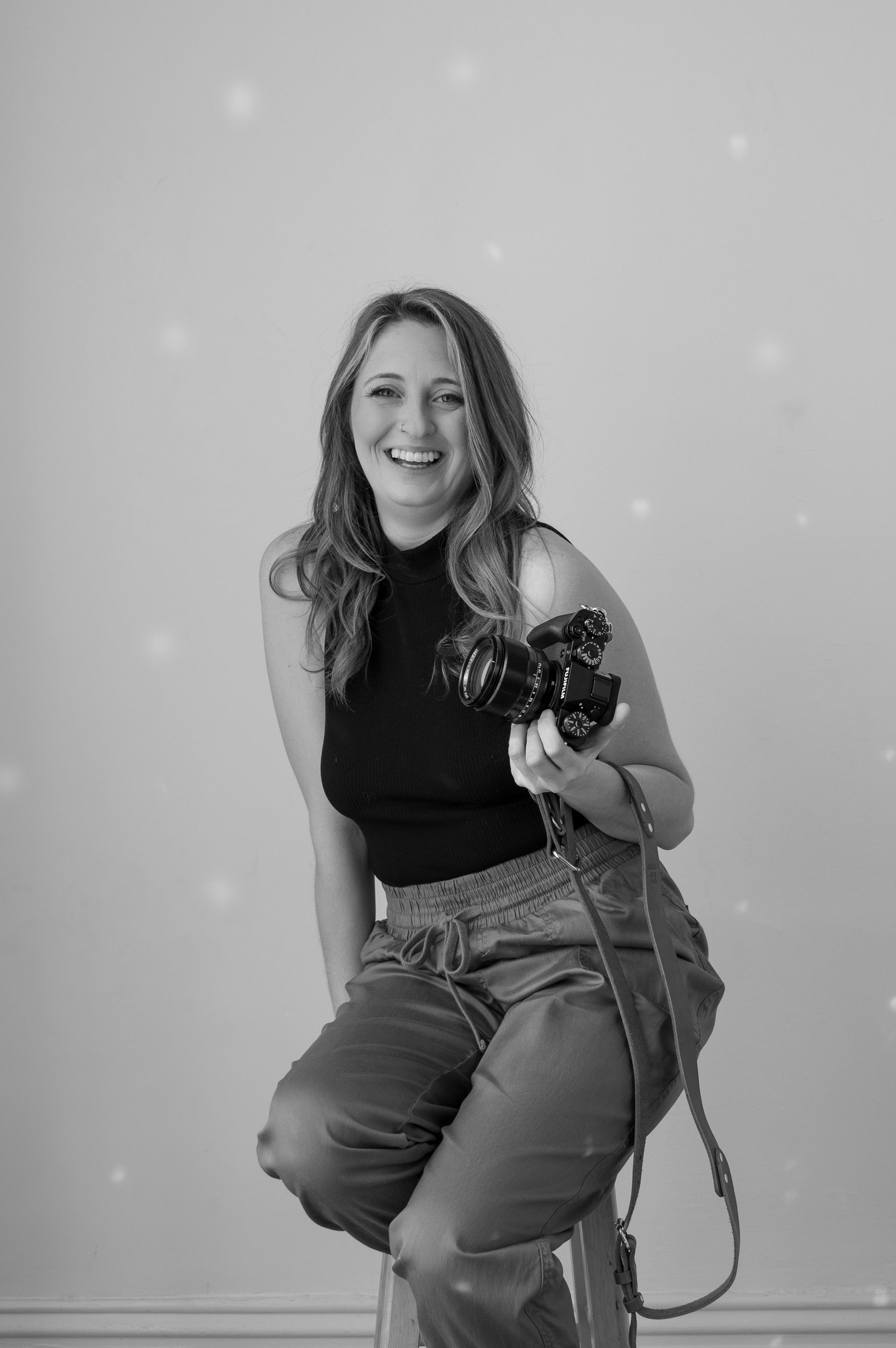 A woman is sitting on a stool holding a camera.