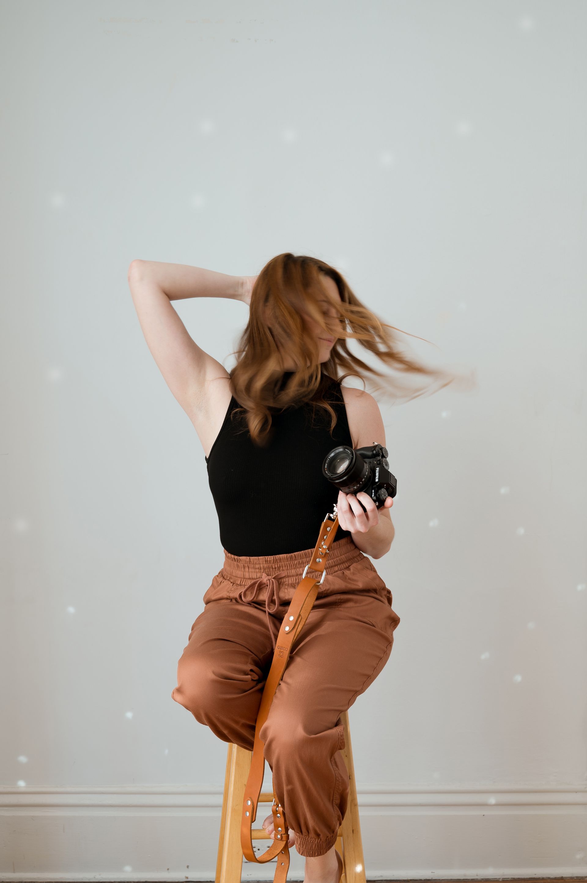A woman is sitting on a stool holding a camera.